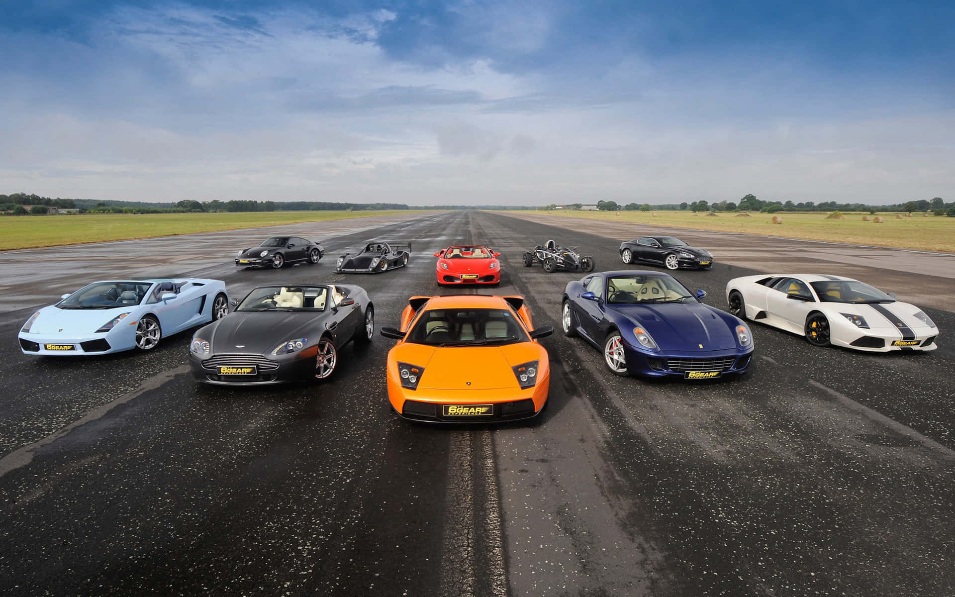 Racing 桌布 壁紙 — 十輛高性能超級跑車以鮮豔色彩排列在潮濕的跑道上，天空部分多雲。