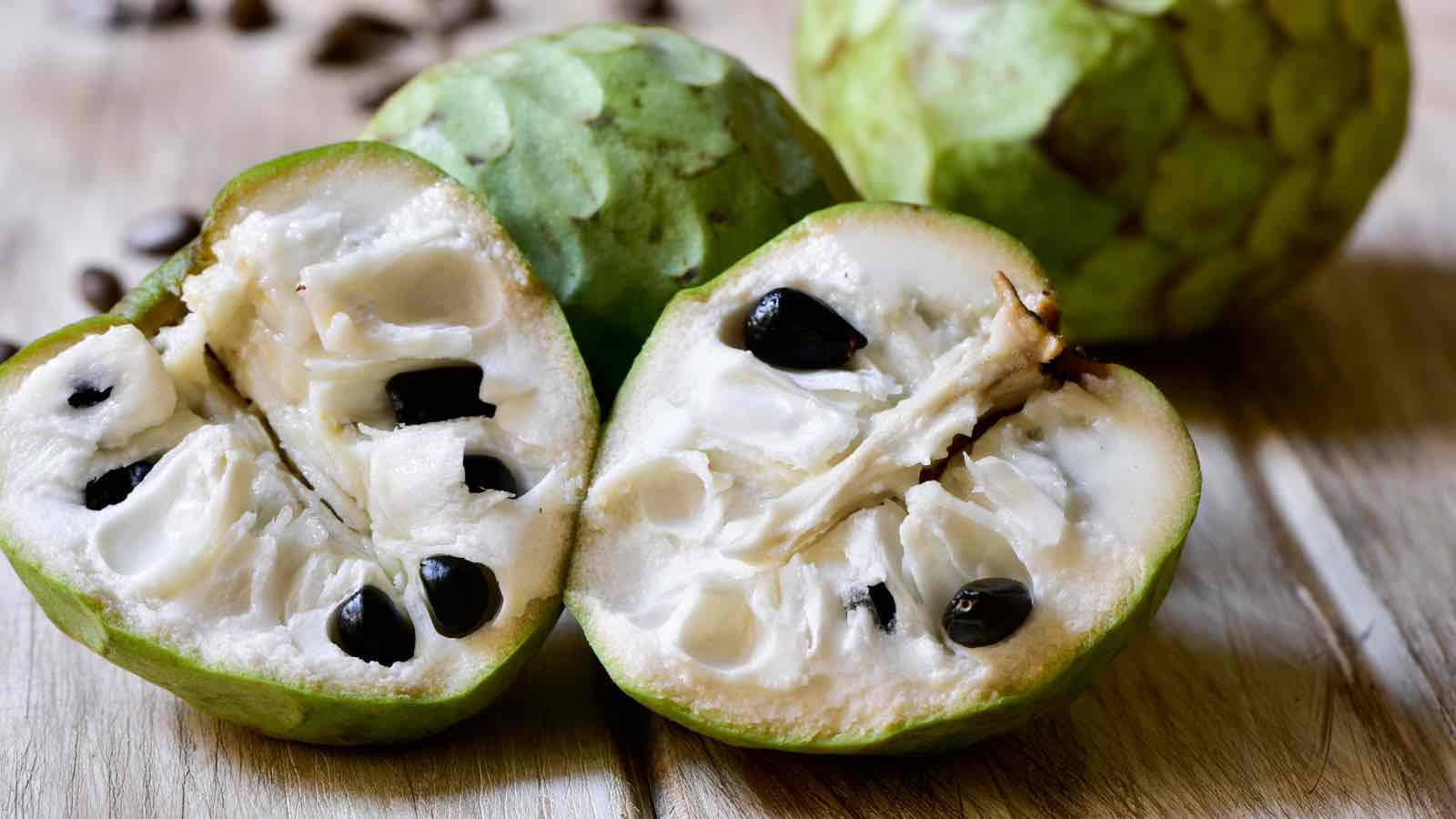 Fruit 桌布 壁紙 — 半個切開的釋迦露出奶油白色果肉和光澤黑色種子，放在木質表面上，完整果實處於柔焦狀態。