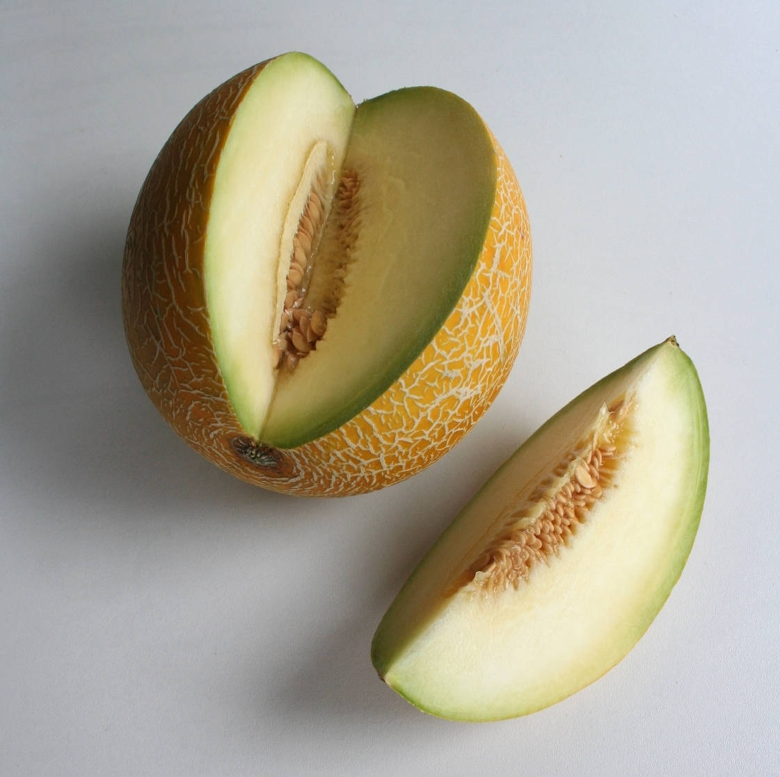 Fruits 桌布 壁紙 — 半個哈密瓜，帶有淡橙色果肉和可見的種子，旁邊放著一片，置於純白表面上。