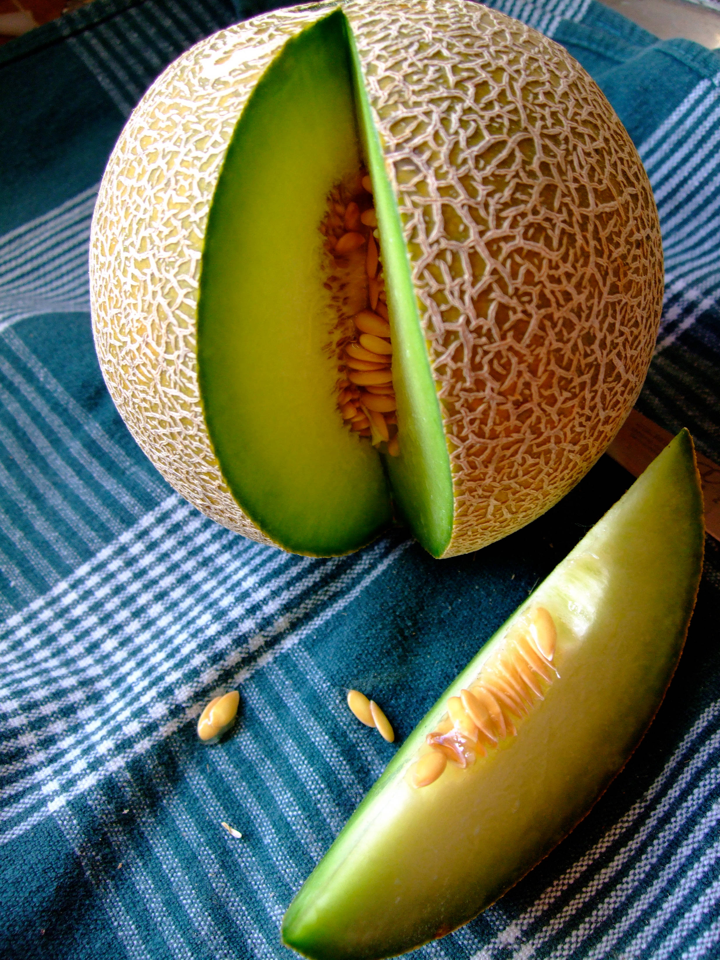 Fruits 桌布 壁紙 — 半個哈密瓜，帶有鮮綠色果肉和種子，放在藍色條紋布上，旁邊有一片瓜。