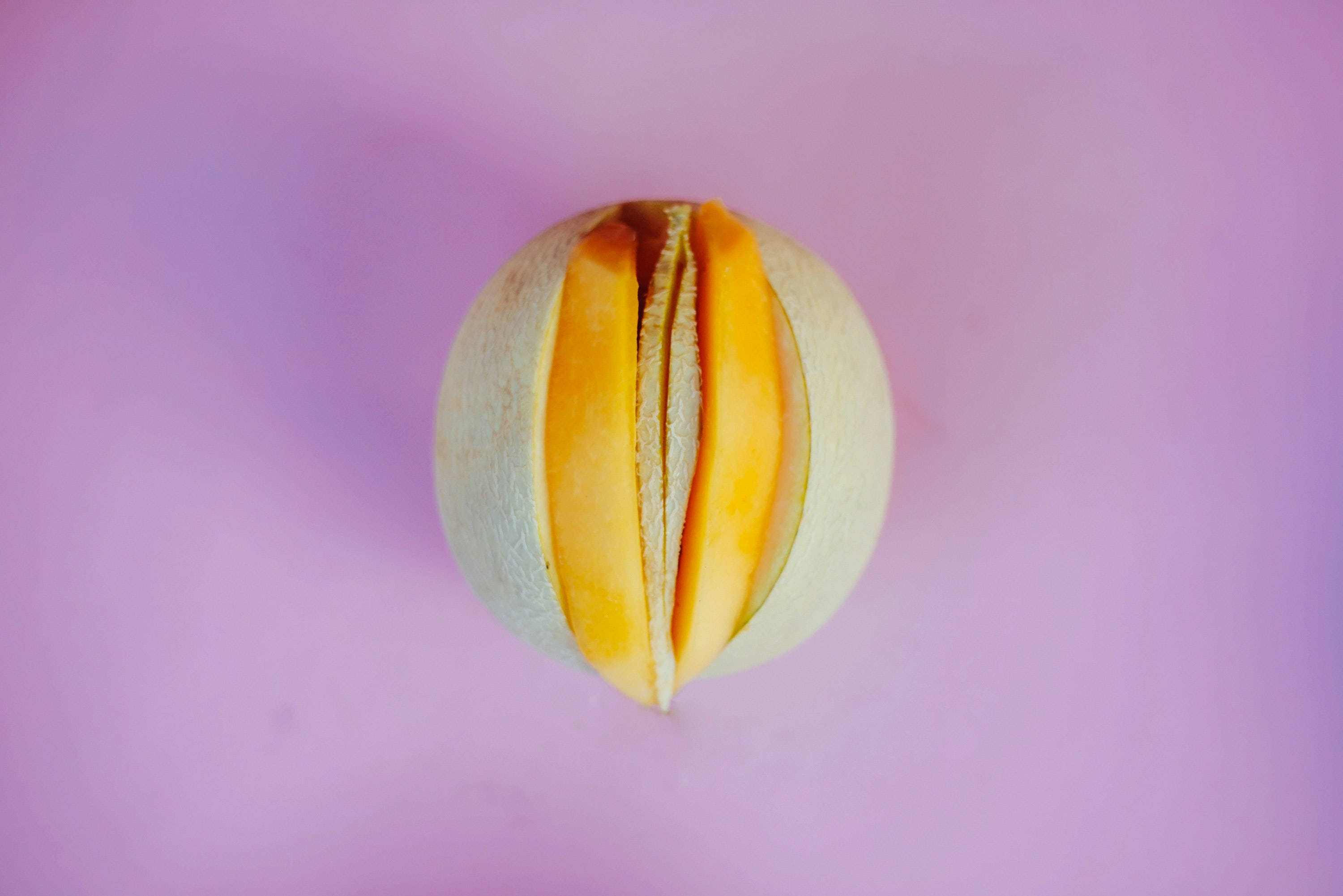 Fruit 桌布 壁紙 — 半個哈密瓜露出多汁的橙色果肉，襯托著柔和的漸變粉紅色背景。