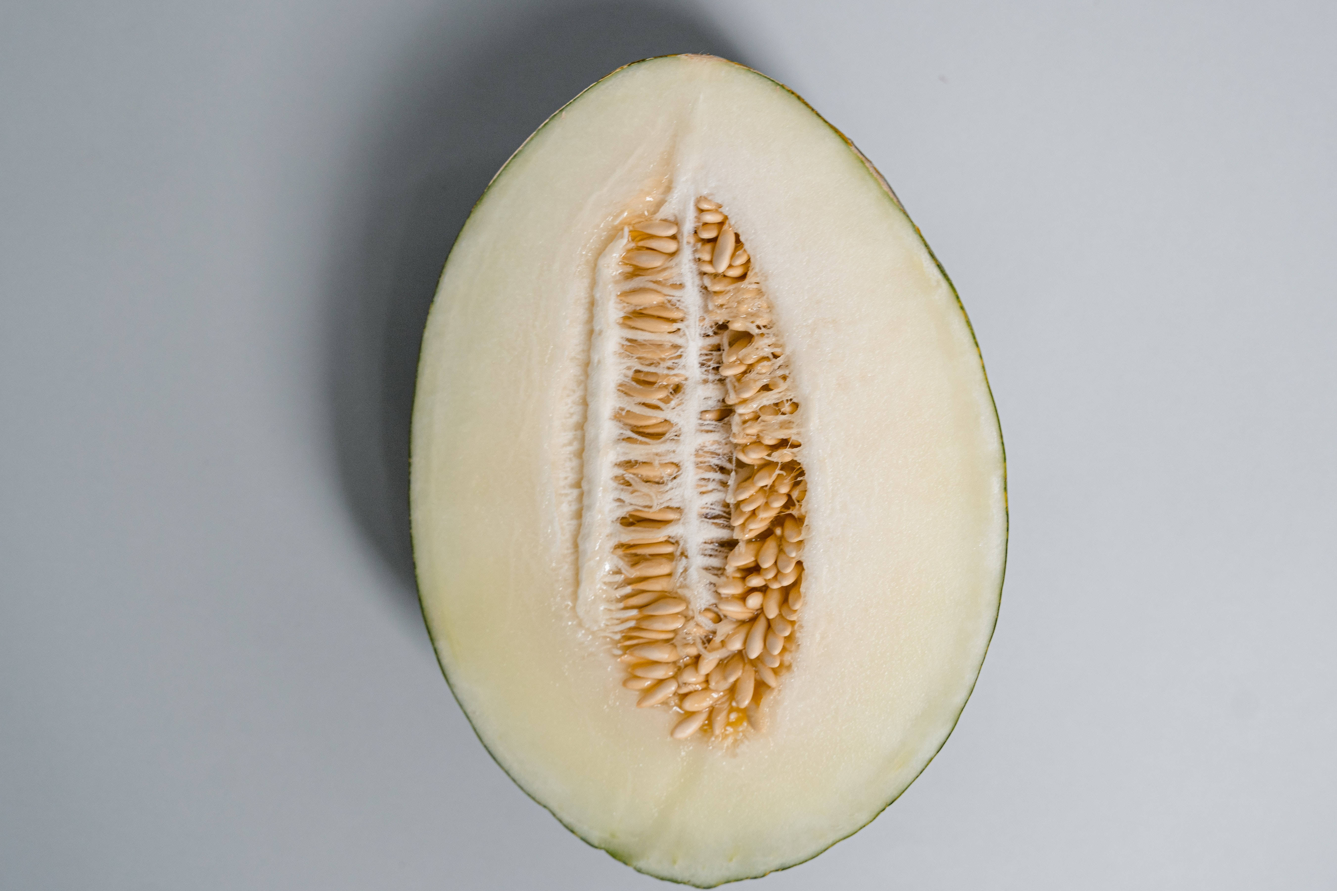 Fruits 桌布 壁紙 — 半個哈密瓜露出淡色果肉和聚集的種子，背景為中性灰色。