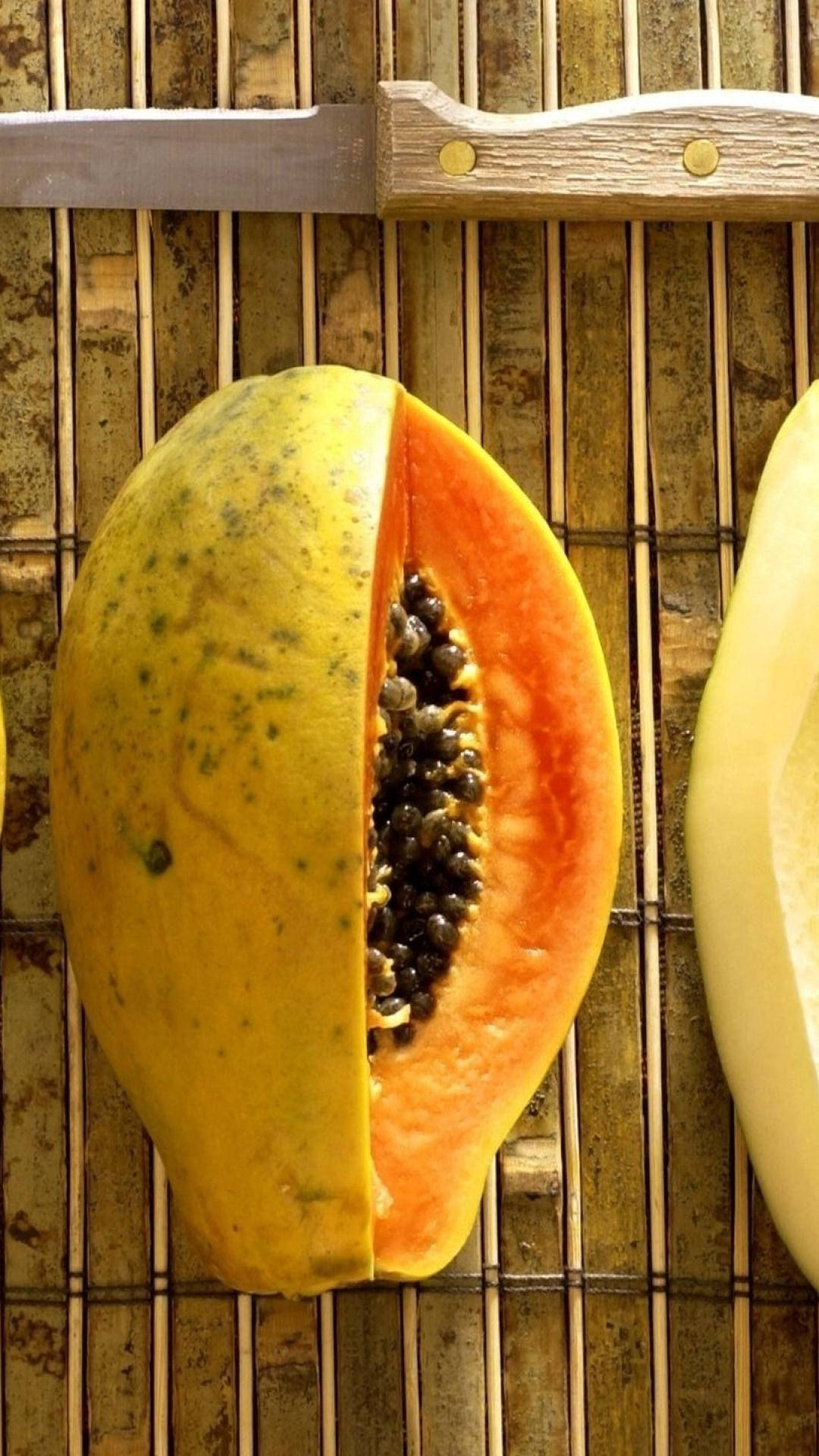Fruit 桌布 壁紙 — 半個木瓜，帶黑色種子和橙色果肉，放在竹蓆上，旁邊有刀和剝下的皮。