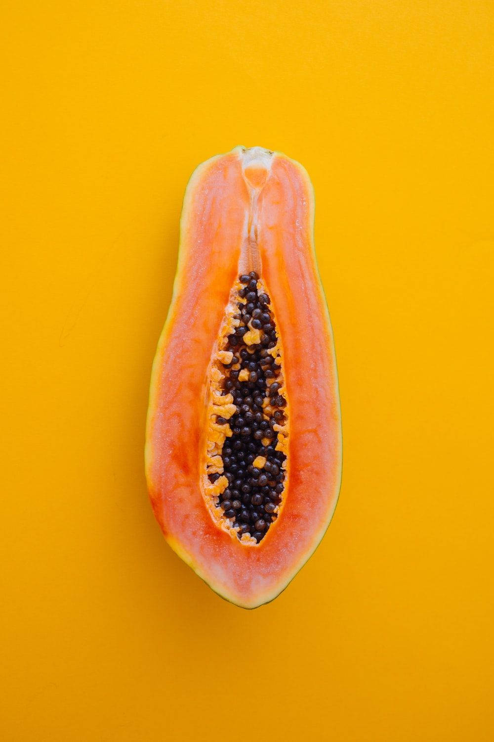 Fruit 桌布 壁紙 — 半個木瓜，橙色果肉和黑色種子，放在鮮黃色背景上。