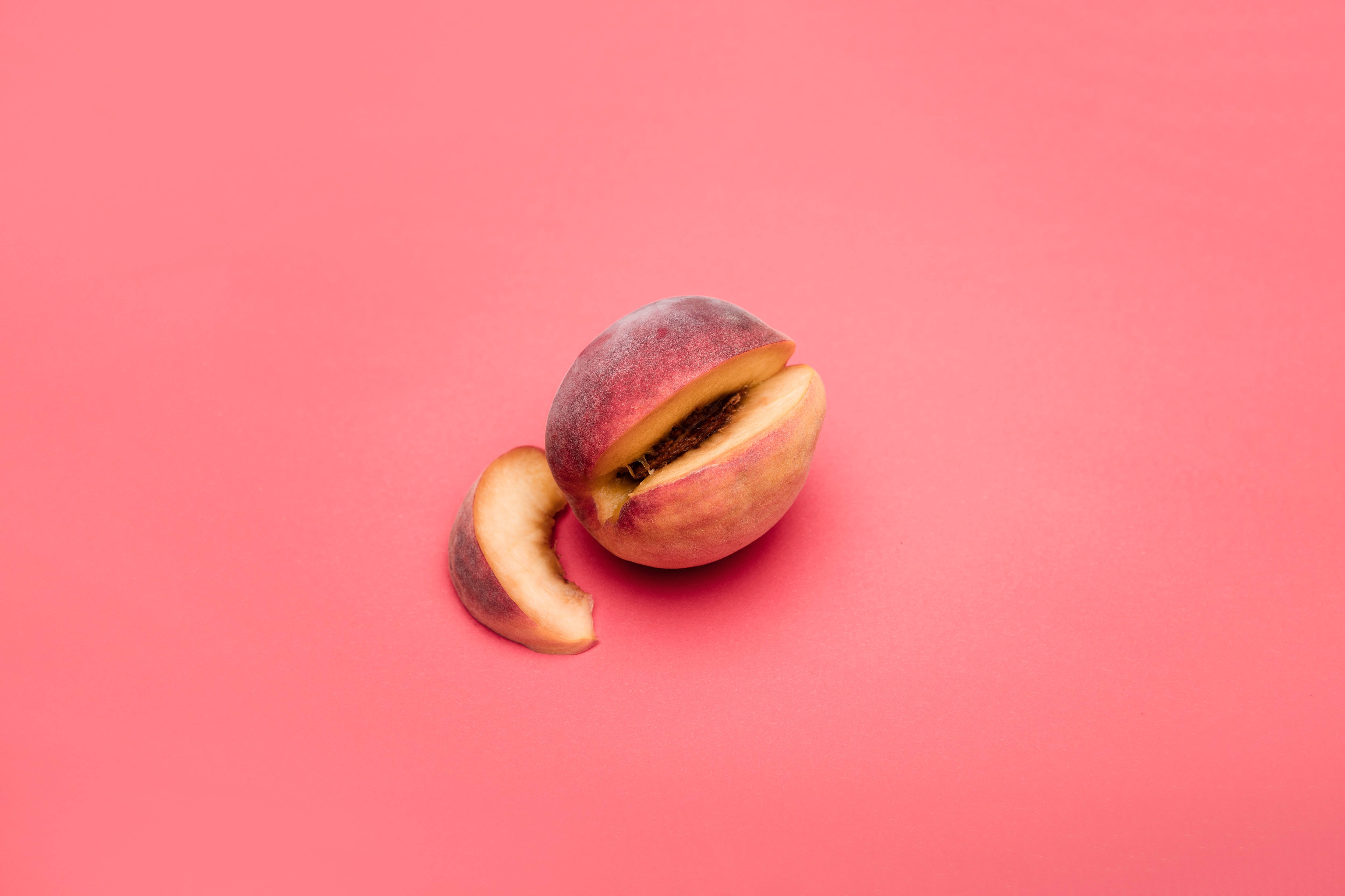 Peach 桌布 壁紙 — 半個桃子旁邊放著一片，置於純珊瑚粉紅背景上。