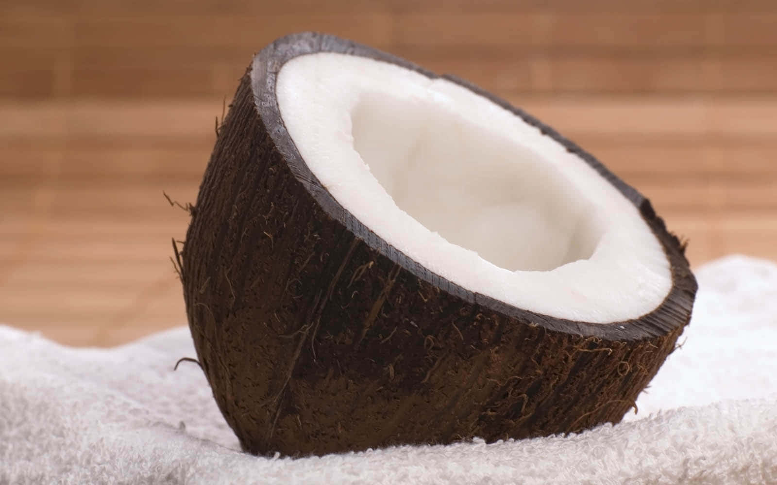 Coconut 桌布 壁紙 — 半個椰子，帶有奶油般的白色果肉，放在白色毛巾上，背景是溫暖的木質。