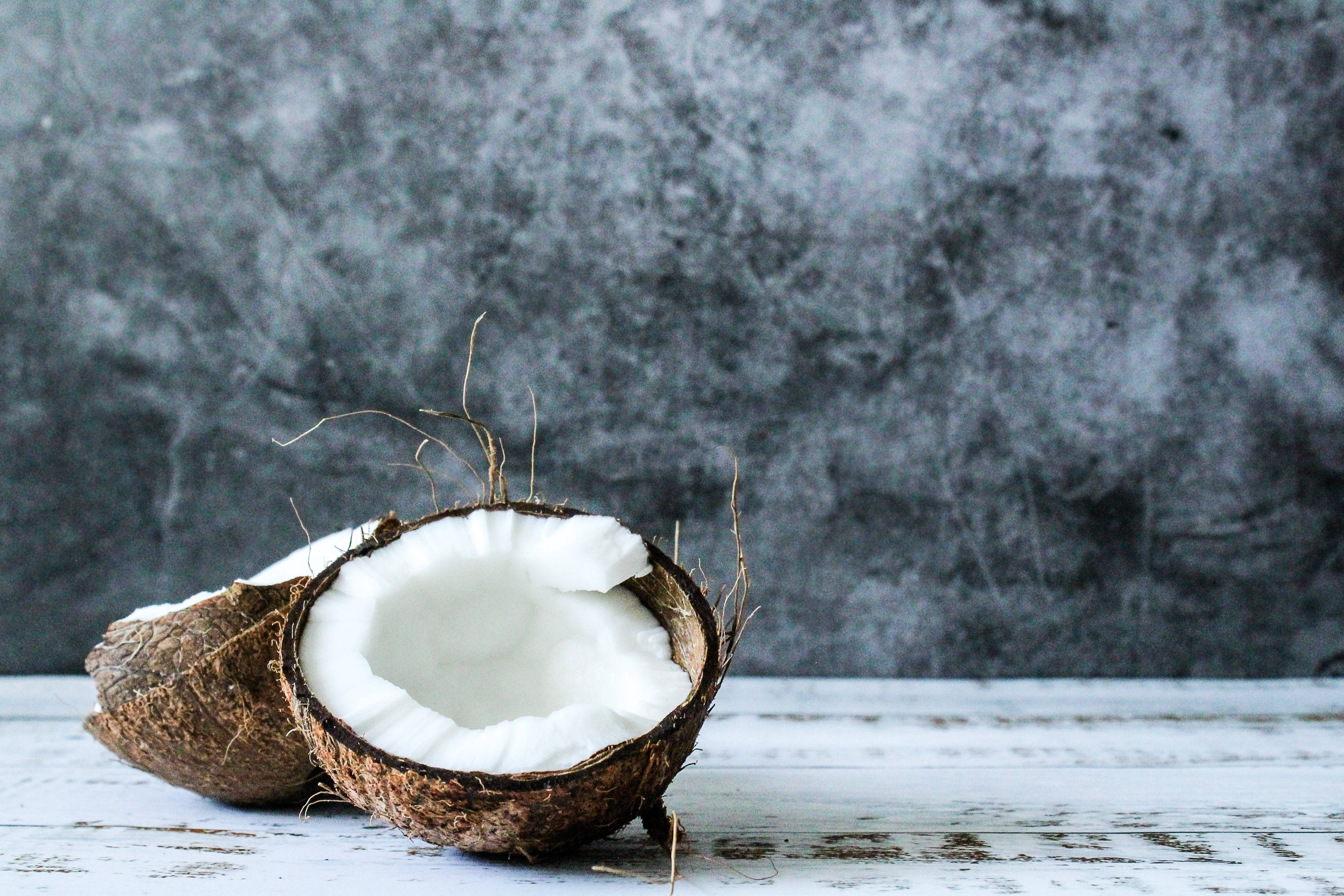 Coconut 桌布 壁紙 — 半個椰子，帶有白色果肉，放置在一個風化的白色木質表面上，背景是帶有紋理的灰色。