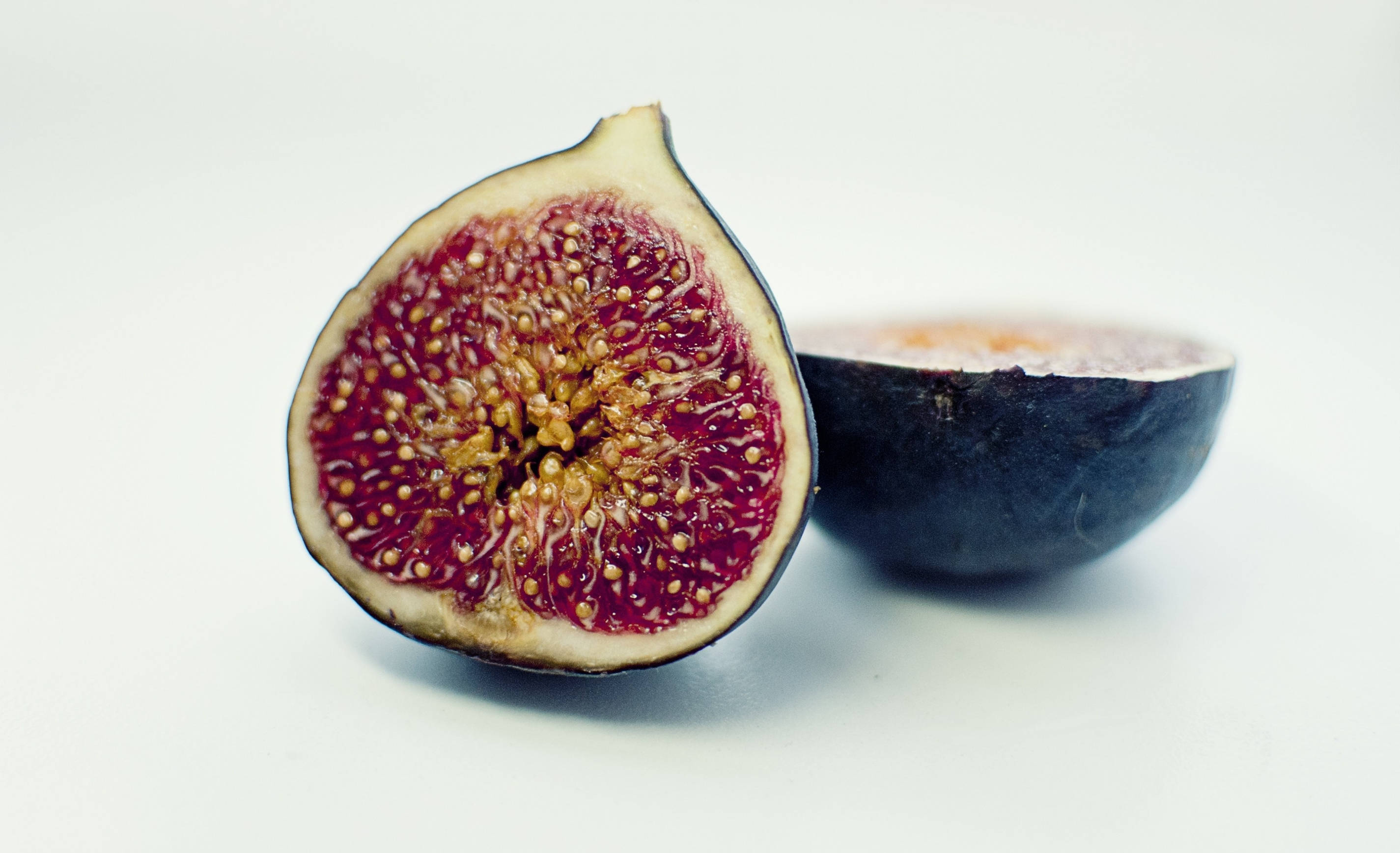 Fruit 桌布 壁紙 — 半個無花果在純白背景下展現出多汁的深紅色果肉和金黃色的種子。
