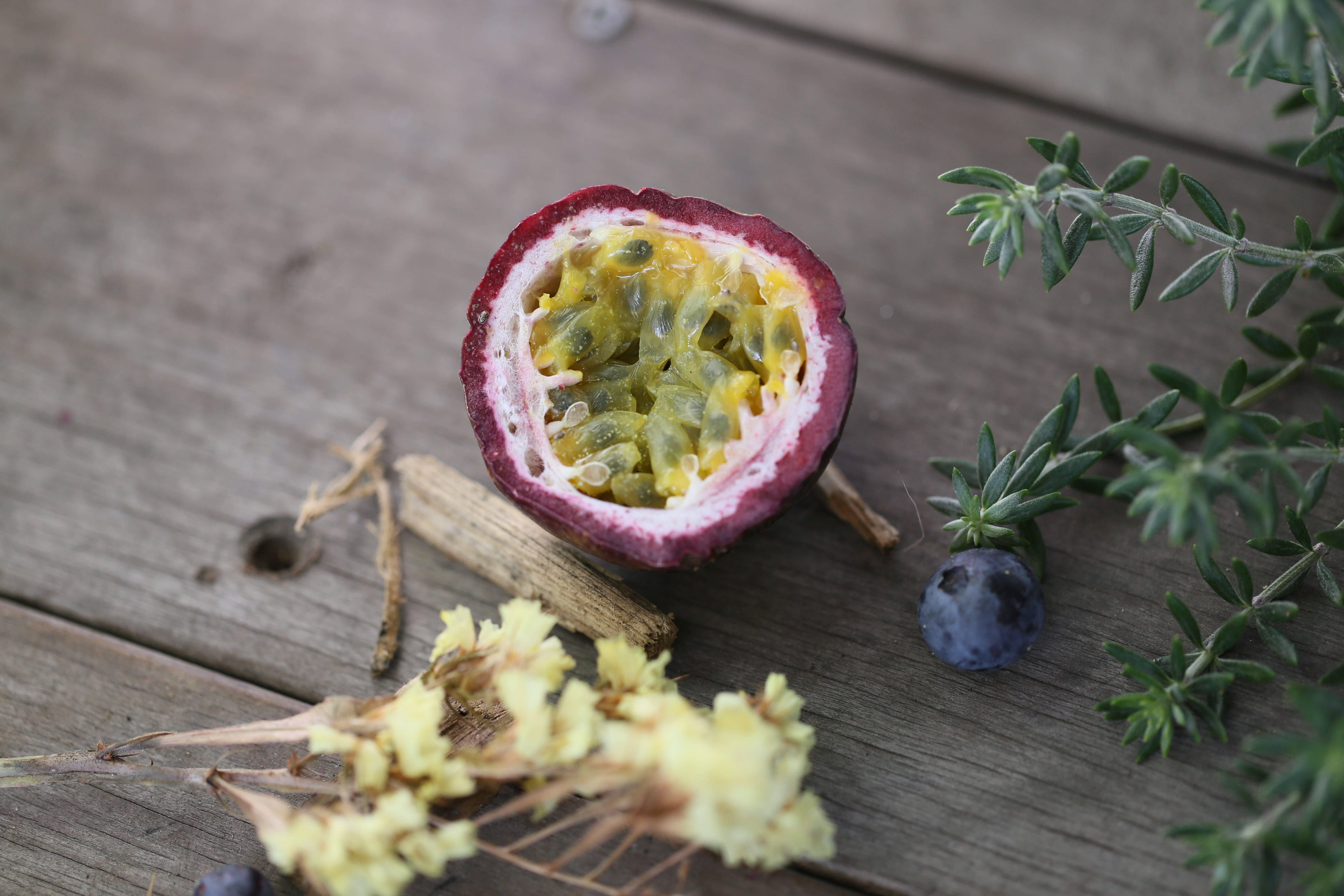 Passion Fruit 桌布 壁紙 — 半個百香果，帶有 juicy 種子，放在經風化的木頭上，旁邊有迷迭香藍莓和乾燥花。