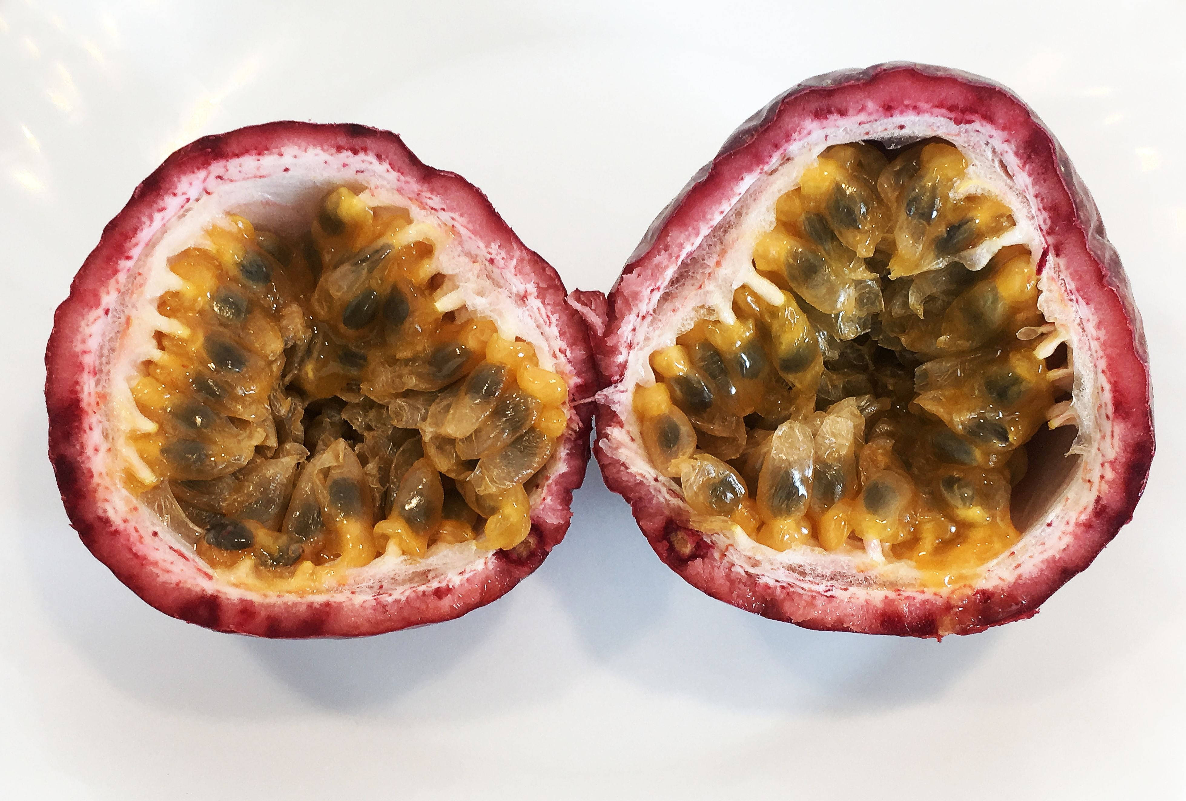 Passion Fruit 桌布 壁紙 — 半個百香果在純白背景下展現多汁的黃色果肉和黑色種子。