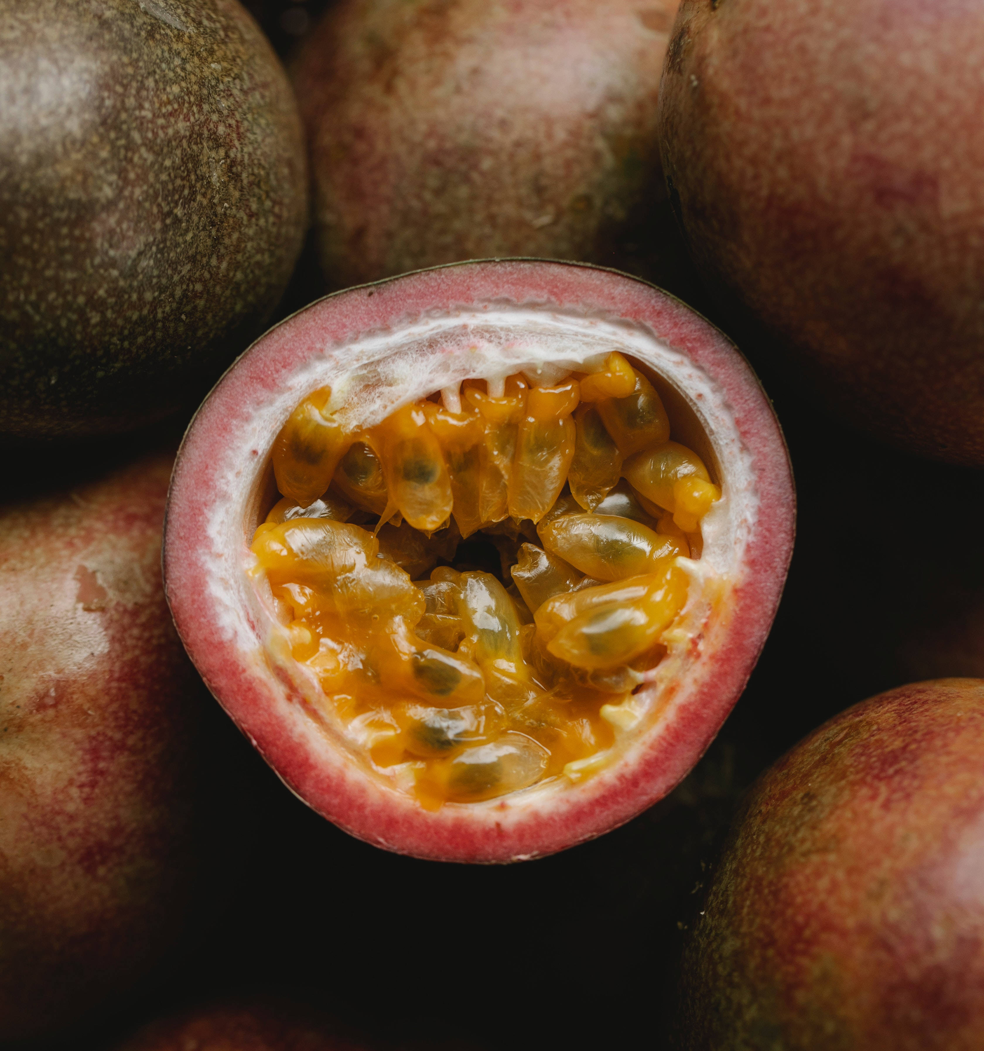 Fruits 桌布 壁紙 — 半個百香果的特寫，露出閃閃發光的金色果肉和種子，周圍環繞著完整的水果。