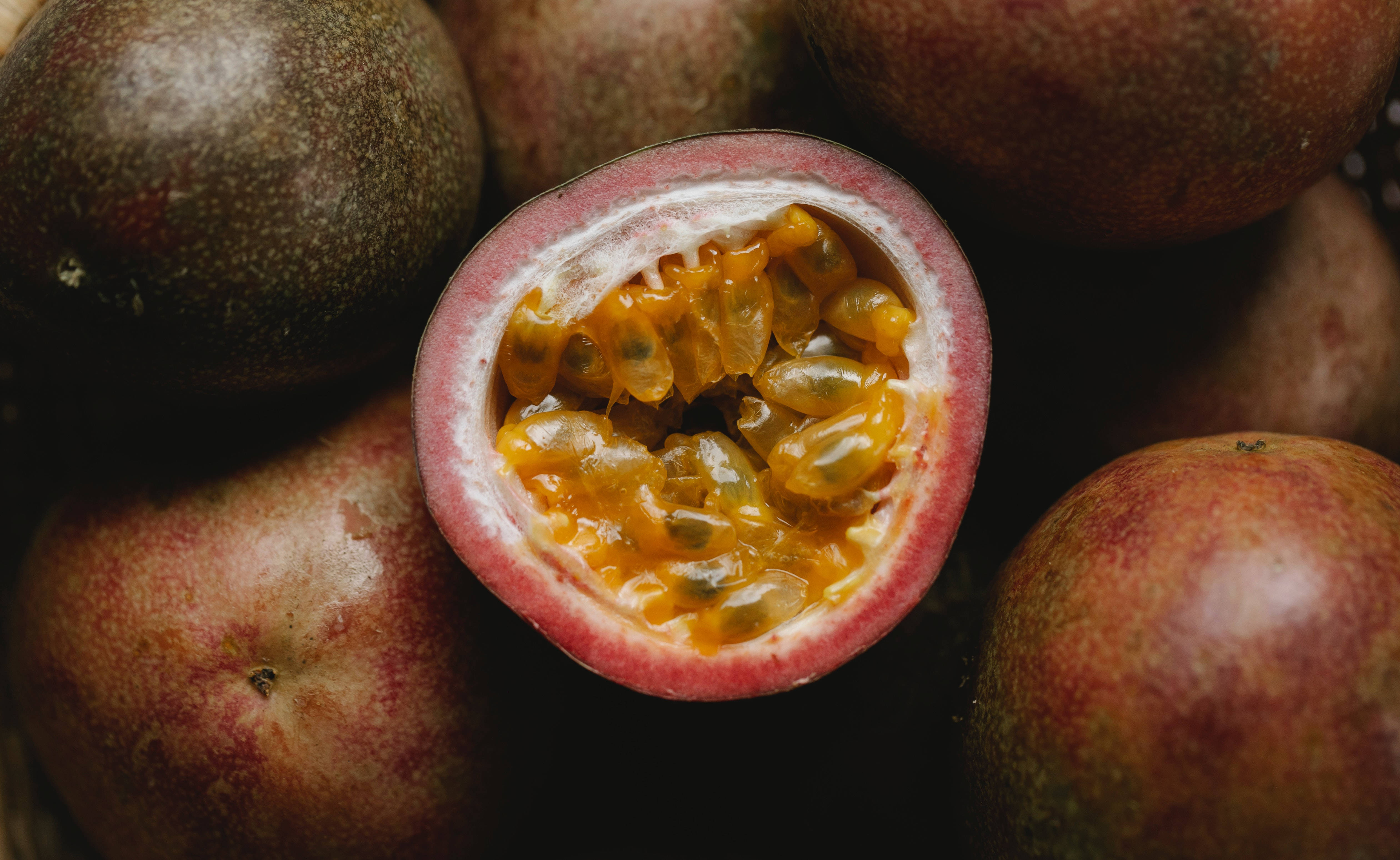 Fruits 桌布 壁紙 — 半個百香果露出閃亮的橙色果肉和種子，與完整果實一起處於柔和焦點中。