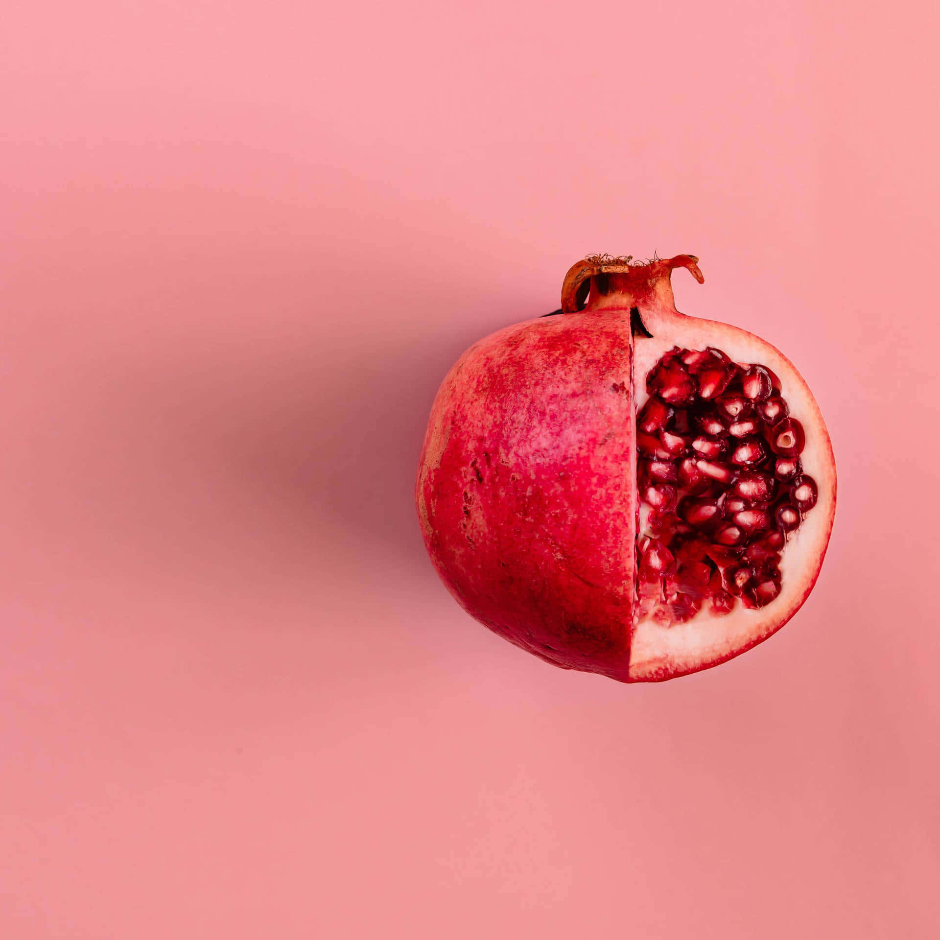 Pastel Red Aesthetic 桌布 壁紙 — 半個石榴露出多汁的紅色籽，襯以柔和的粉紅色背景。