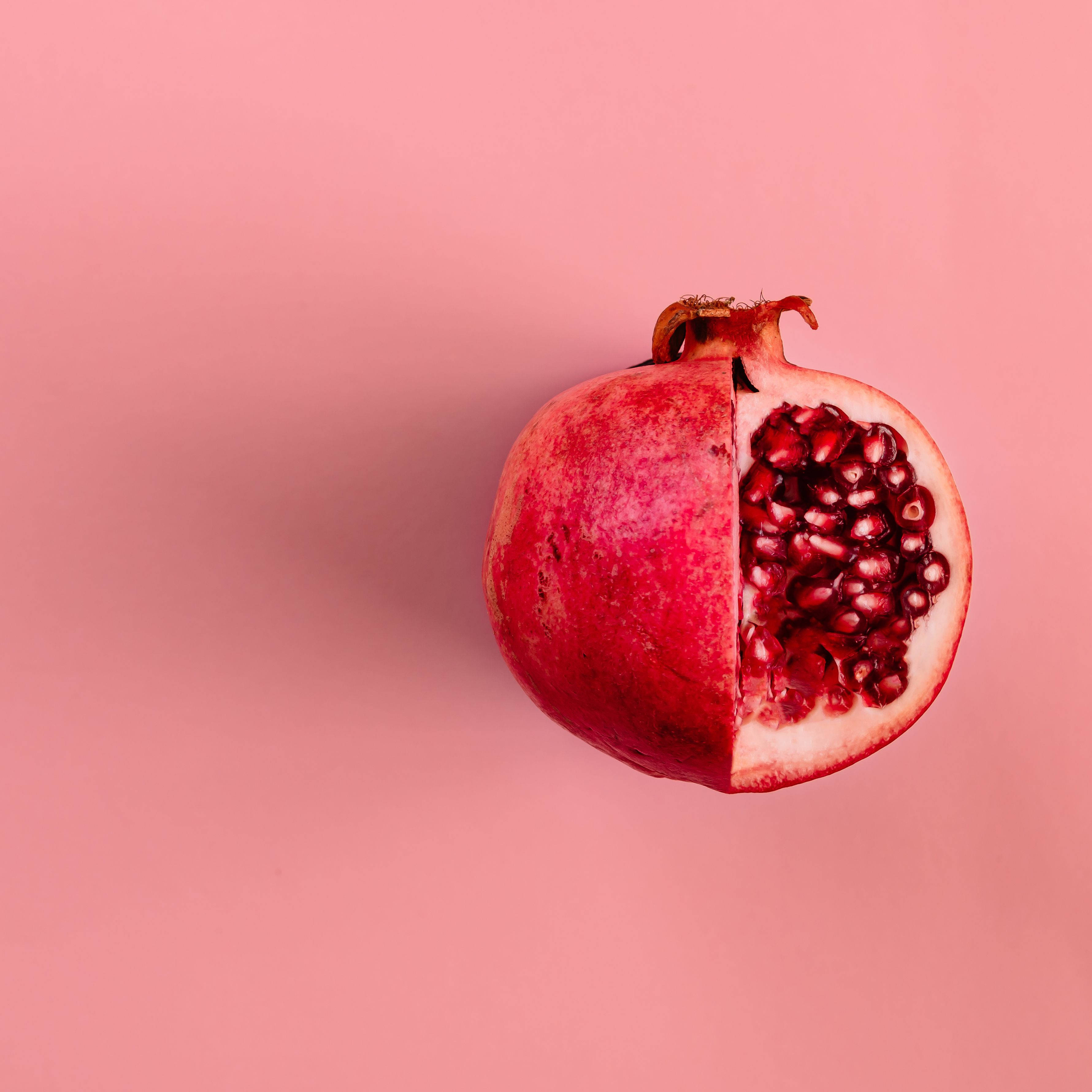 iPhone 桌布 壁紙 — 半個石榴露出多汁的紅色籽，襯托著柔和的粉紅色背景。