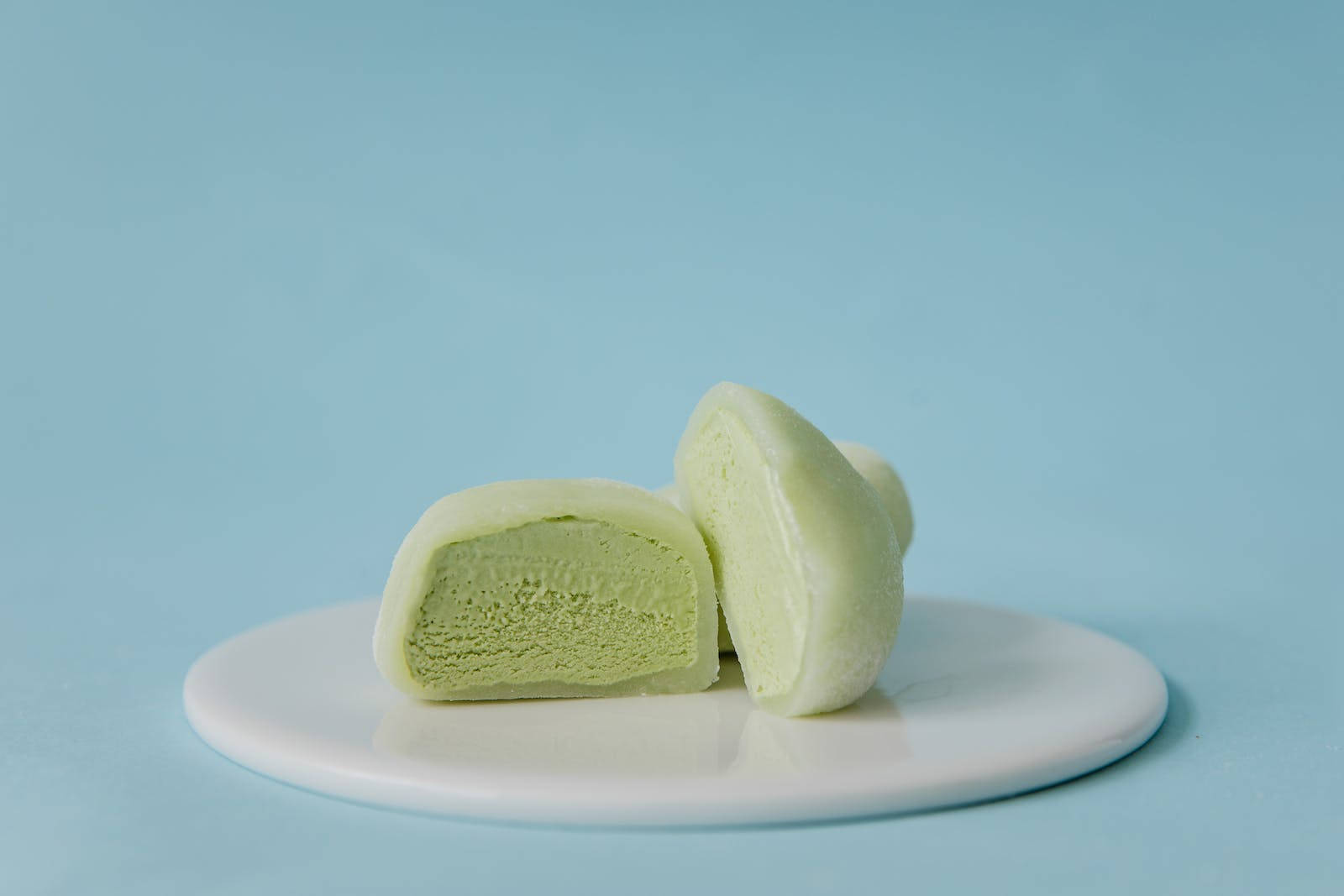 Mochi 桌布 壁紙 — 半個綠色抹茶麻糬甜點放在白色盤子上，背景是柔和的藍色。
