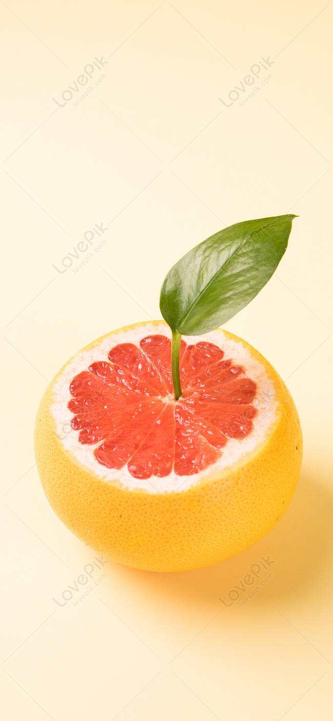 Fruit 桌布 壁紙 — 半個葡萄柚，帶有鮮紅色果肉和新鮮綠葉放在黃色果皮上，背景為柔和奶油色。