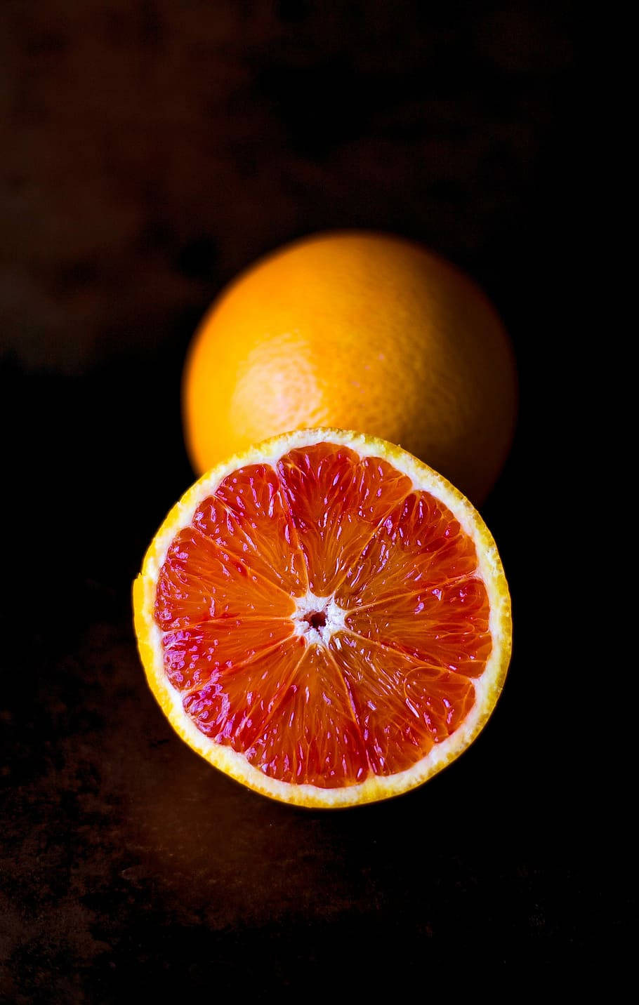 Fruit 桌布 壁紙 — 半個血橙露出鮮紅色的果肉，背景是深色有紋理的表面，後面有一個完整的柳橙。