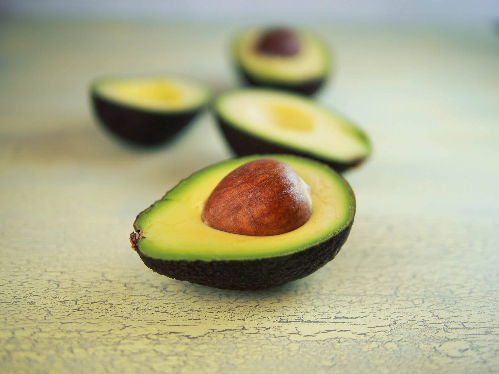 Avocado 桌布 壁紙 — 半個酪梨的特寫，帶有突出的果核，放在風化的黃色表面上。