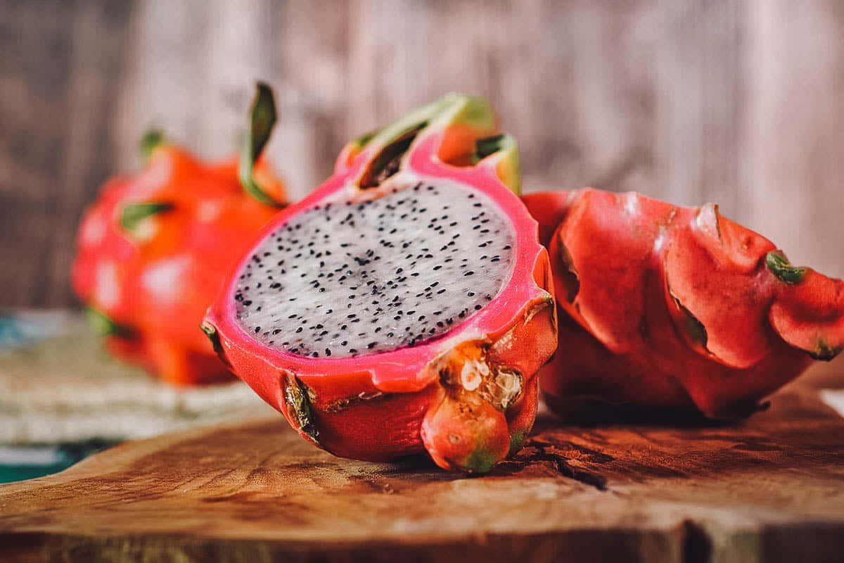 Red Fruit 桌布 壁紙 — 半個鮮豔的火龍果，白色果肉和黑色種子，放在質樸的木板上，旁邊有完整的水果。