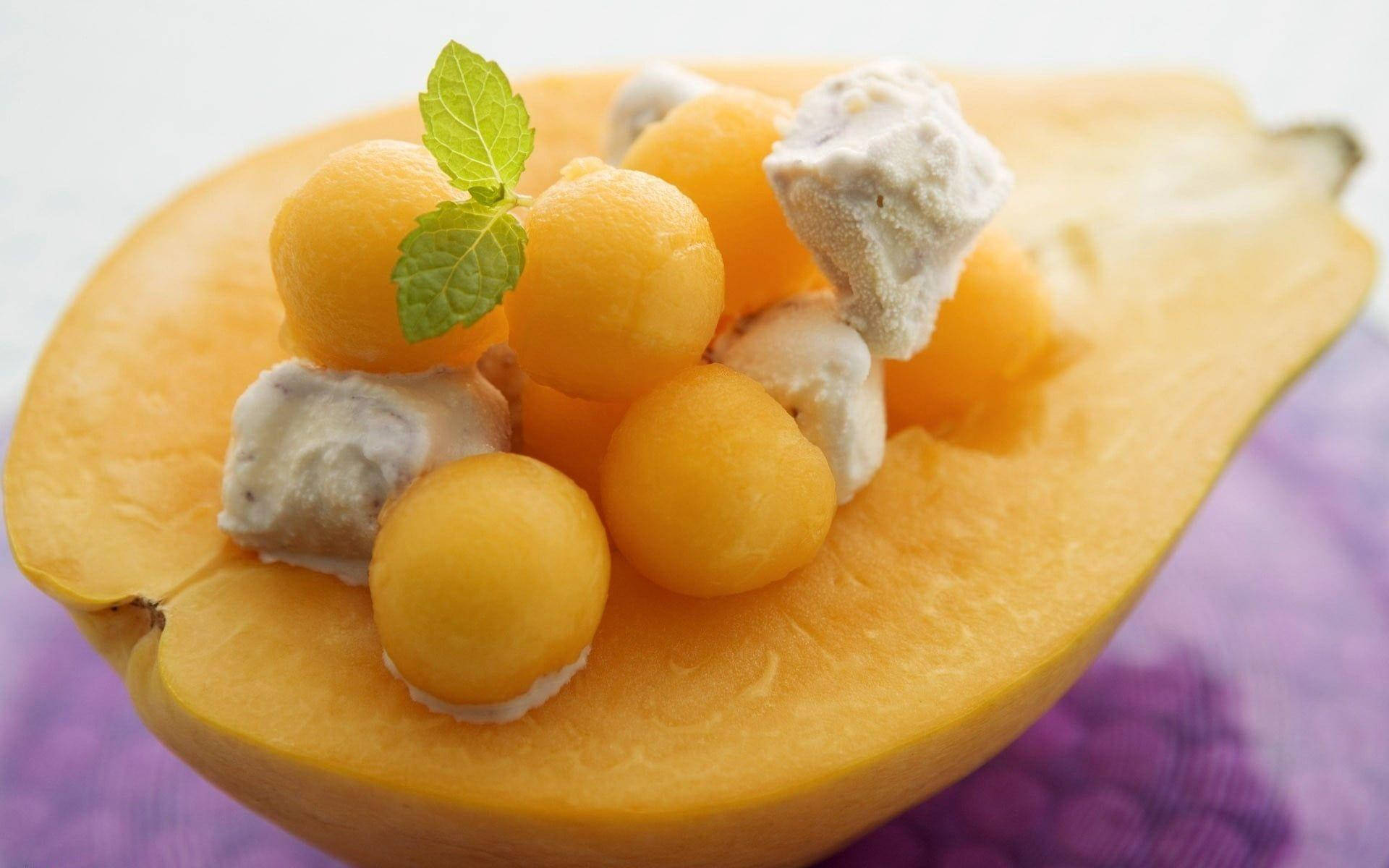 Fruit 桌布 壁紙 — 半個黃色南瓜，裡面裝滿金色蜜瓜球和奶油白色方塊，上面裝飾著新鮮薄荷葉。