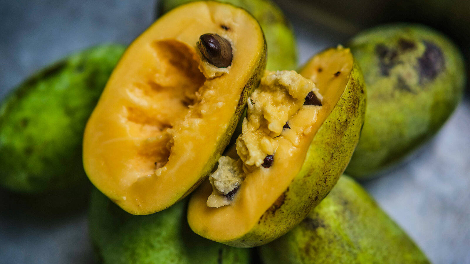 Fruit 桌布 壁紙 — 半切泡泡果的特寫，露出其奶油黃色果肉和被綠色外皮包圍的深色種子。