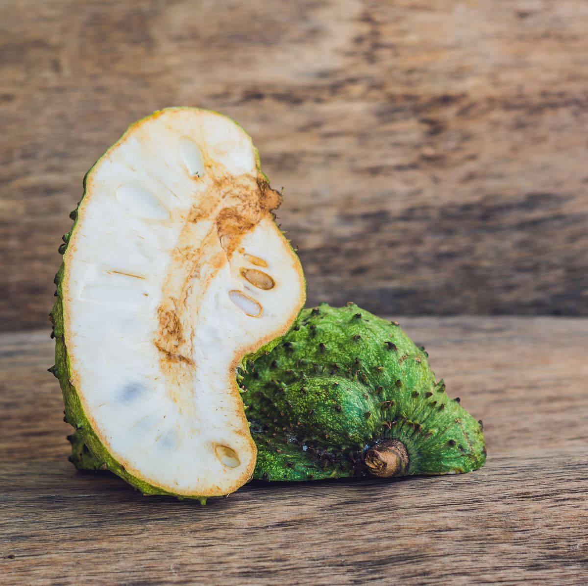Fruits 桌布 壁紙 — 半切的刺果番荔枝在質樸的木質表面上展現出其奶油般的白色果肉和深色種子。