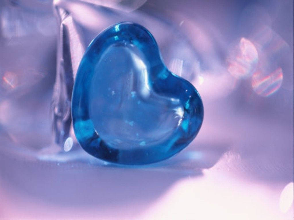 Blue Heart 桌布 壁紙 — 半透明藍色心形玻璃飾品在夢幻的紫色和粉紅色散景背景下閃爍著柔和的光芒。