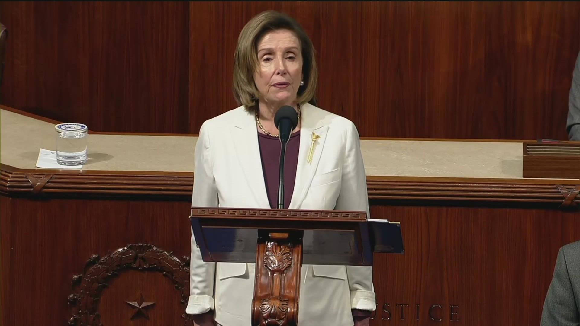 Nancy Pelosi 桌布 壁紙 — 南希·裴洛西站在正式會議廳的木製講台上發表演講，旁邊放著一杯水。