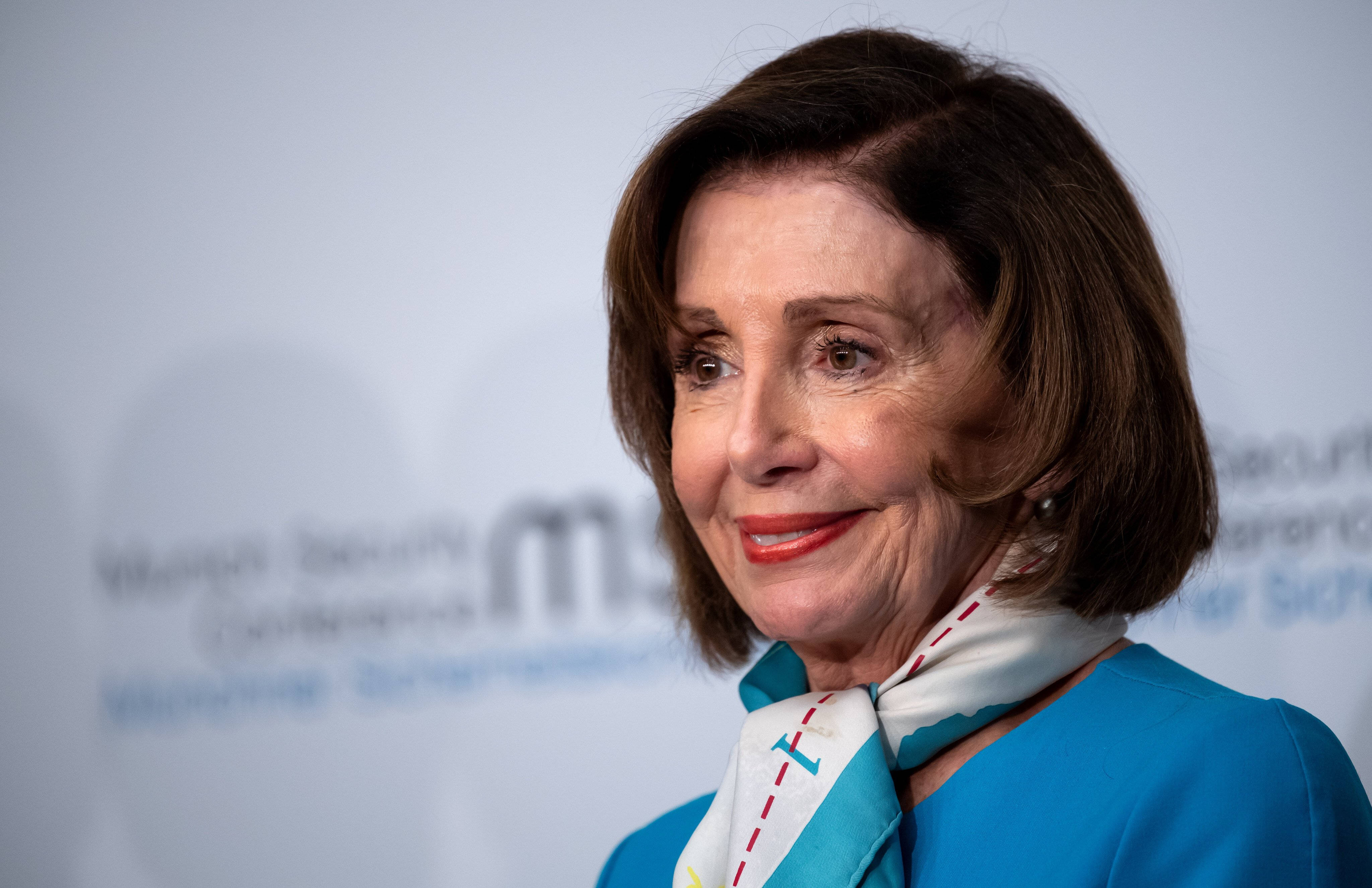 Nancy Pelosi 桌布 壁紙 — 南希·裴洛西身穿藍色西裝和圖案圍巾，在模糊的活動背景下溫暖地微笑。