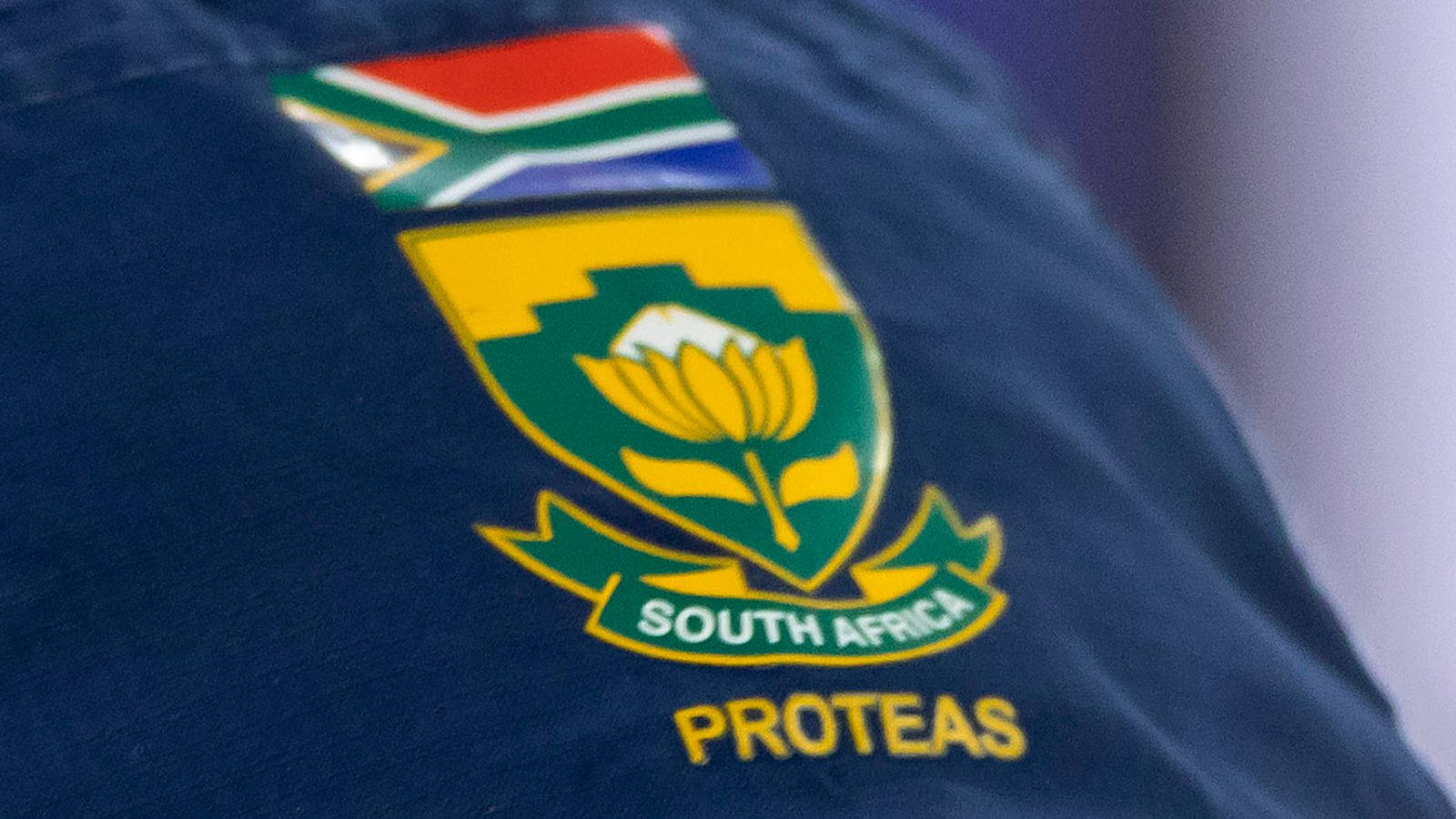south africa cricket 桌布 壁紙 — 南非 Proteas 標誌近距離特寫，繡在深藍色布料上，上方有國旗。
