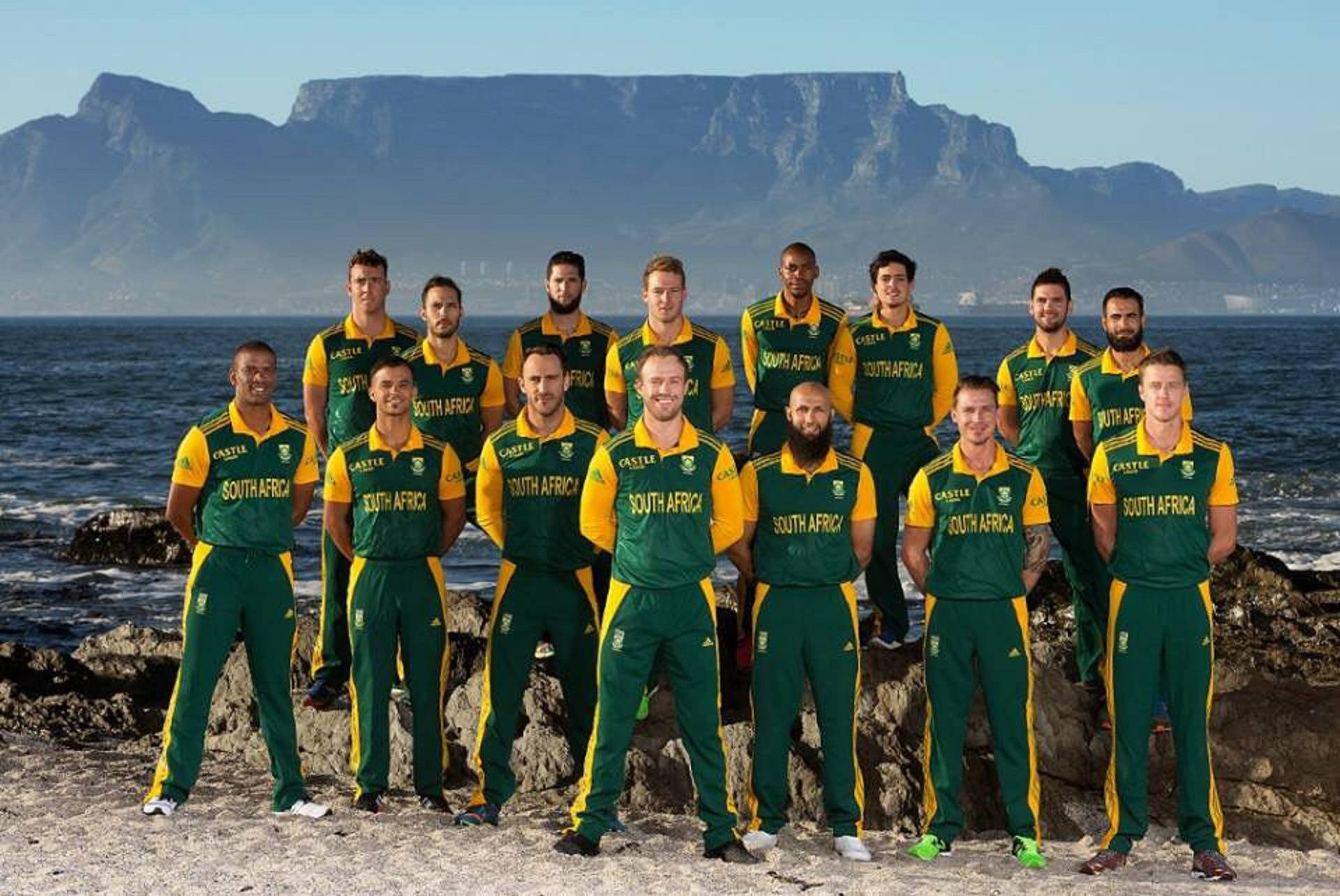 south africa cricket 桌布 壁紙 — 南非板球隊身穿綠色和黃色制服，在岩石海岸懸崖上擺姿勢，背景是桌山。