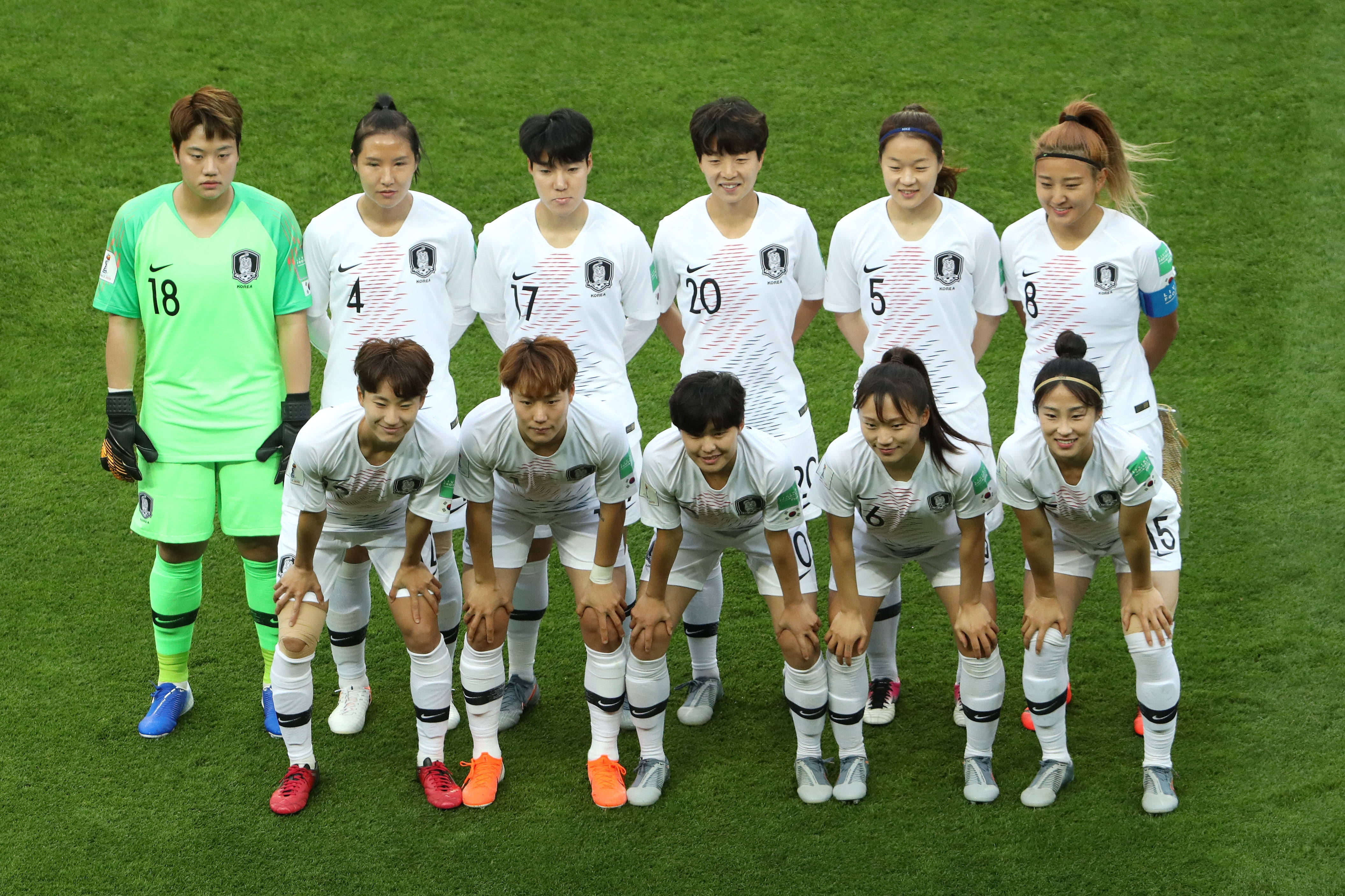 Football Players 桌布 壁紙 — 南韓女子足球隊在充滿活力的綠色球場上以陣容擺姿勢，身穿白色和螢光綠色球衣。