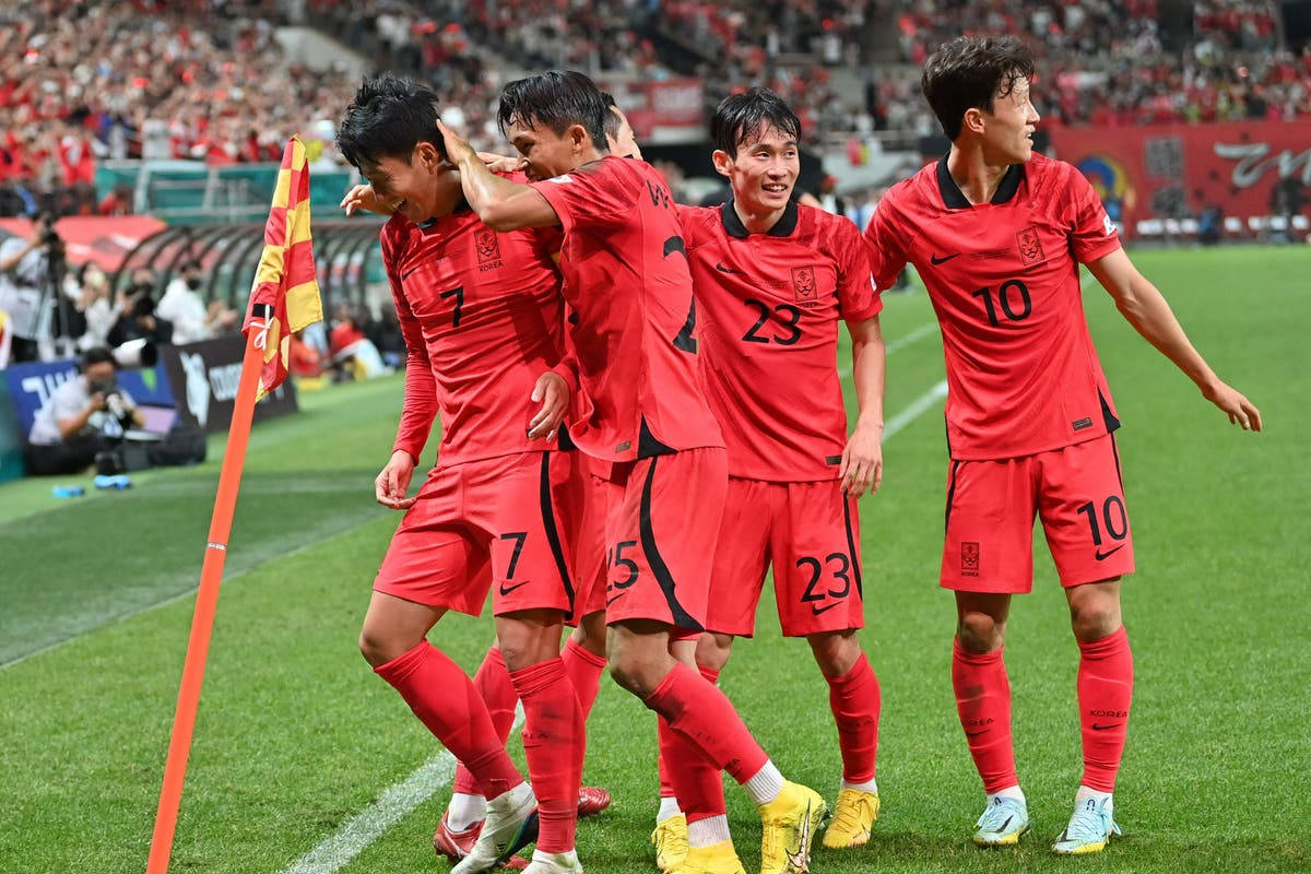 Football Players 桌布 壁紙 — 南韓足球運動員身穿紅色球衣，在充滿活力的綠色球場上以喜悅的擁抱慶祝進球。