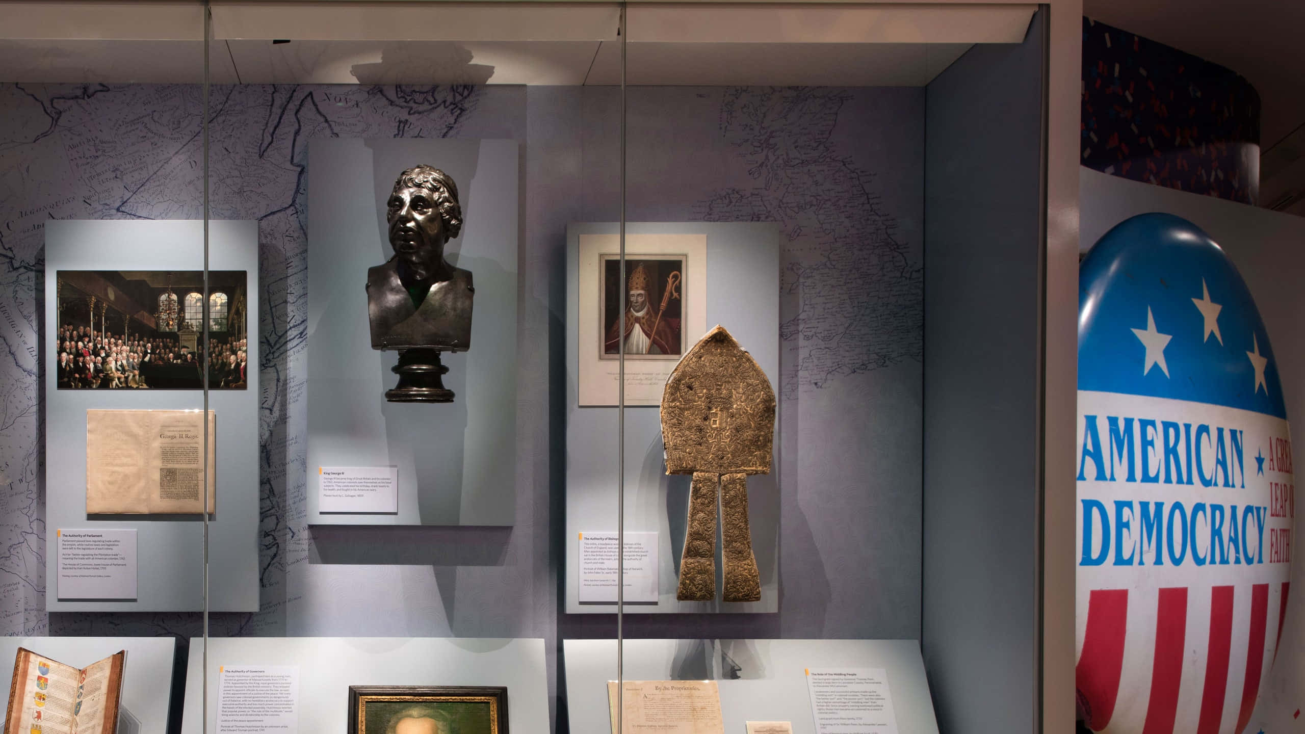 history 桌布 壁紙 — 博物館展覽展示歷史文物，包括半身肖像、裱框照片和一個大型American Democracy氣球，背景為地圖壁紙。
