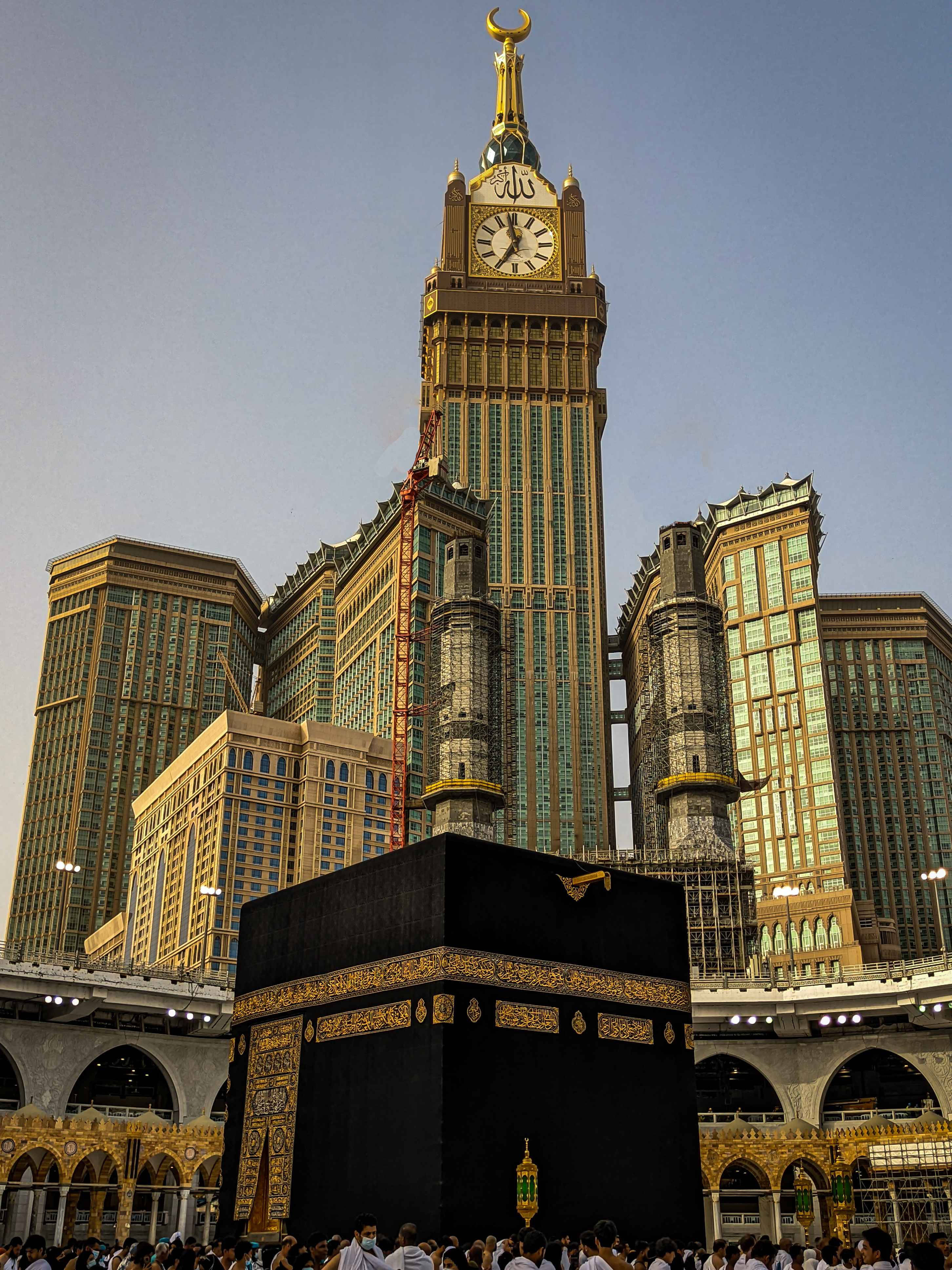 Makkah 桌布 壁紙 — 卡巴天房莊嚴地矗立在麥加，周圍是高聳的金色摩天大樓，頭頂是清澈的藍天。