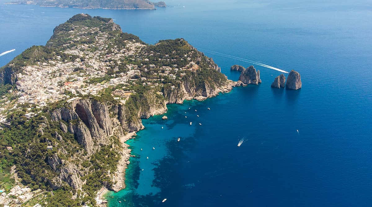 Italian Island 桌布 壁紙 — 卡布里島的鳥瞰圖，碧綠海水、船隻和陽光下標誌性的法拉廖尼岩石。