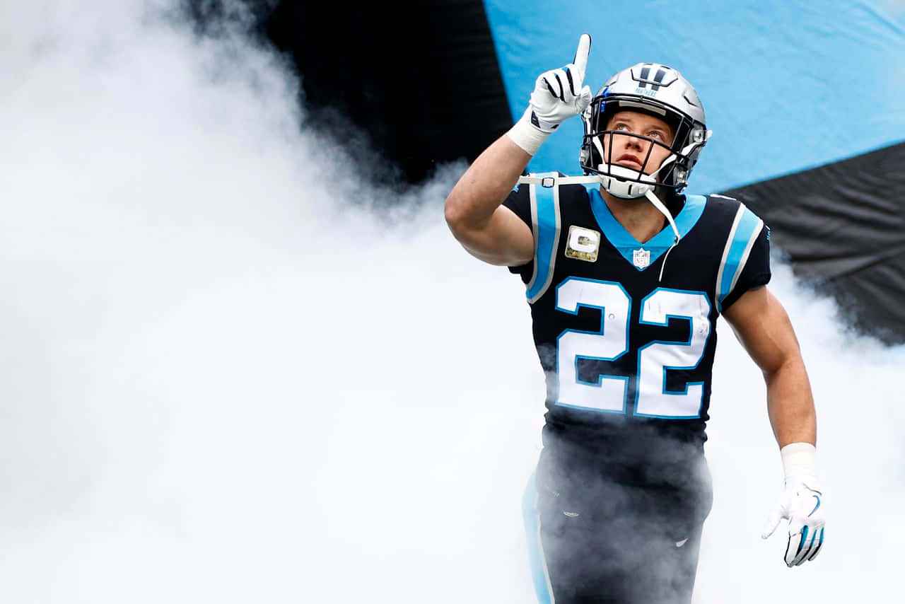Christian Mccaffrey 桌布 壁紙 — 卡羅萊納黑豹隊22號球衣的足球員從煙霧中出現，堅定地向上指。