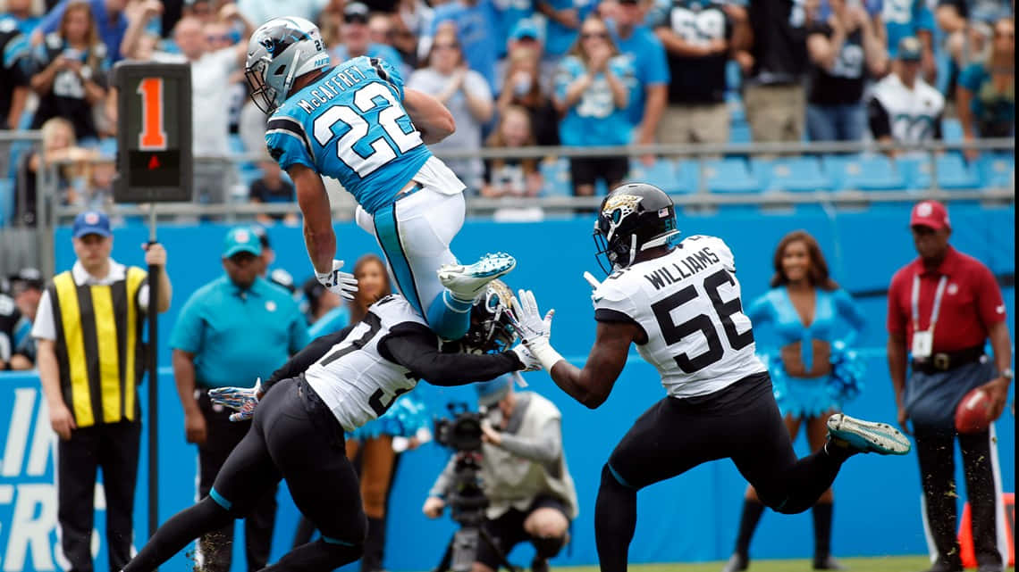 Christian Mccaffrey 桌布 壁紙 — 卡羅萊納黑豹隊球員在半空中跳起接住美式足球，而兩名傑克遜維爾美洲虎隊防守球員在日間比賽中逼近。