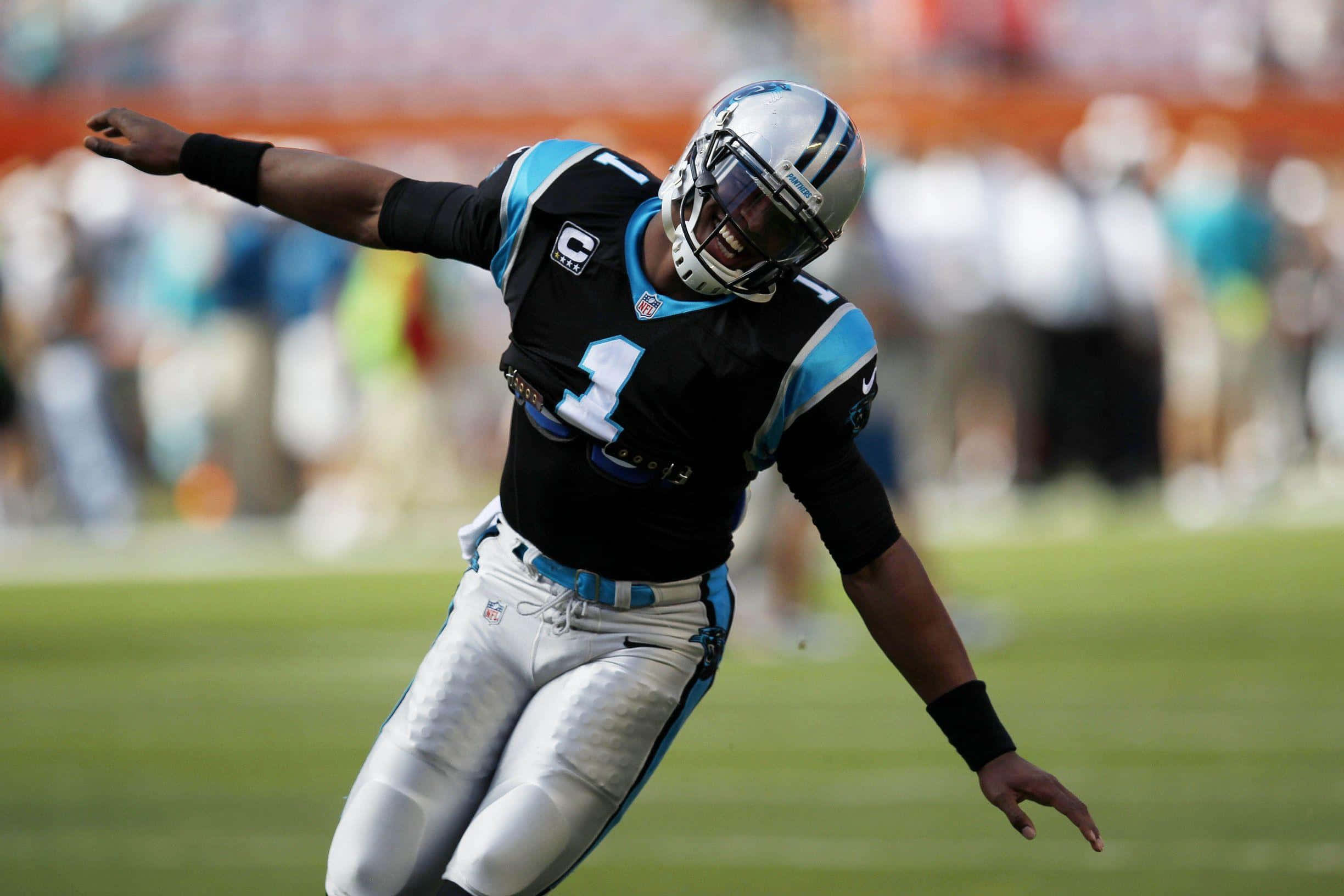 Cam Newton 桌布 壁紙 — 卡羅萊納黑豹隊的四分衛身穿黑藍色球衣，在陽光明媚的足球場上張開雙臂慶祝。