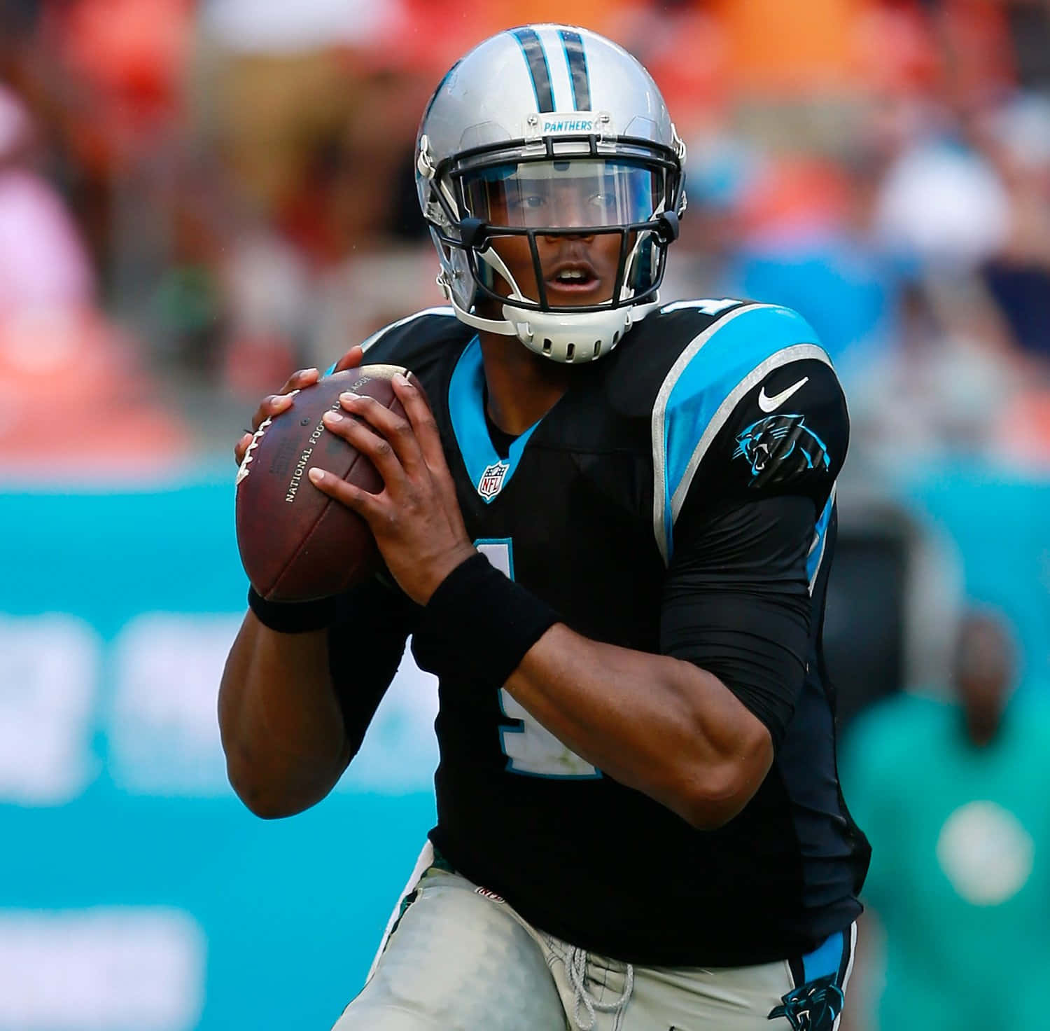 Cam Newton 桌布 壁紙 — 卡羅萊納黑豹隊的四分衛身穿黑藍色球衣，在明亮的球場燈光下於比賽中抓住一個橄欖球。