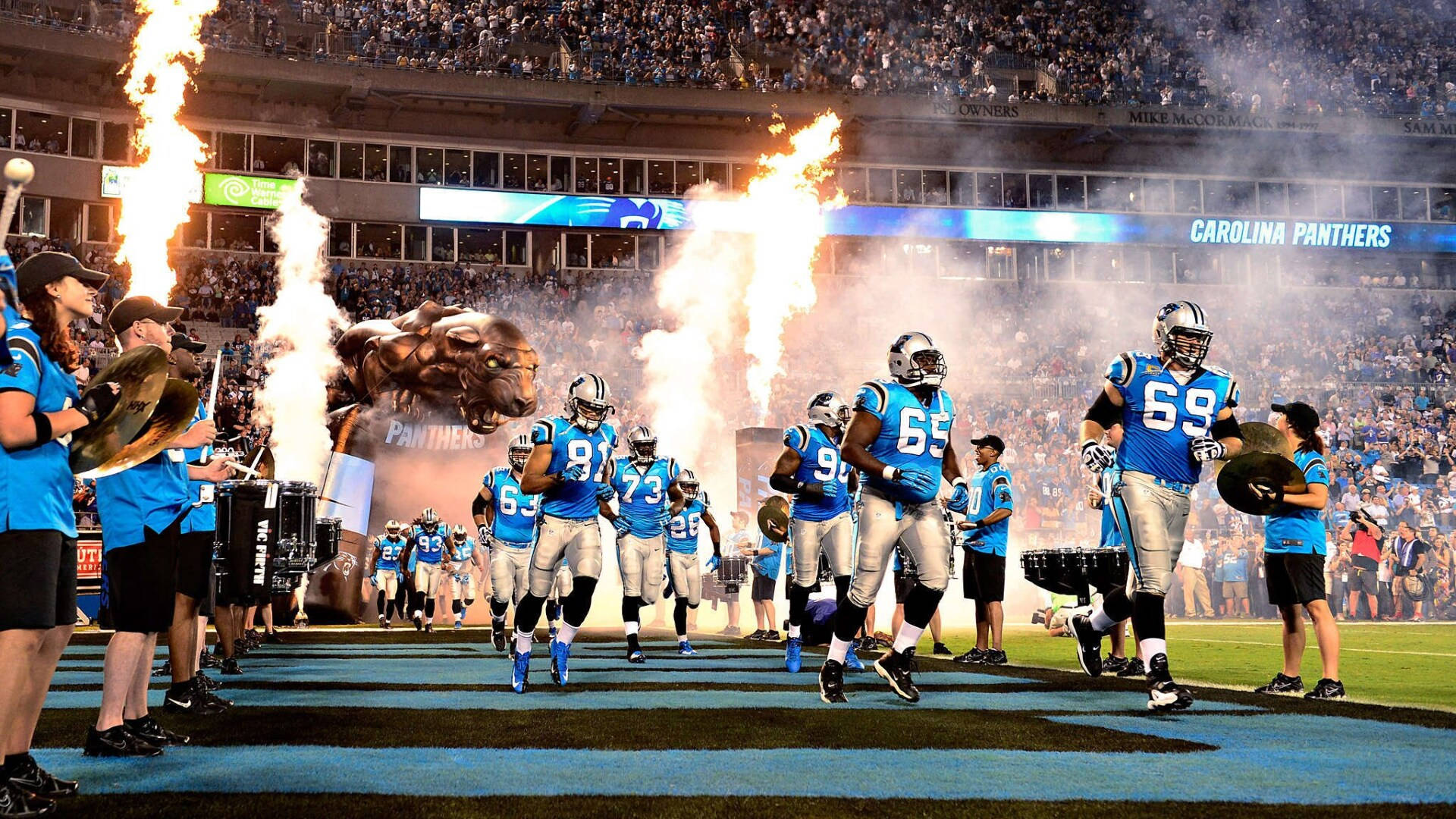 Panthers 桌布 壁紙 — 卡羅萊納黑豹隊的足球員在火焰和煙霧中跑進擠滿觀眾的球場。