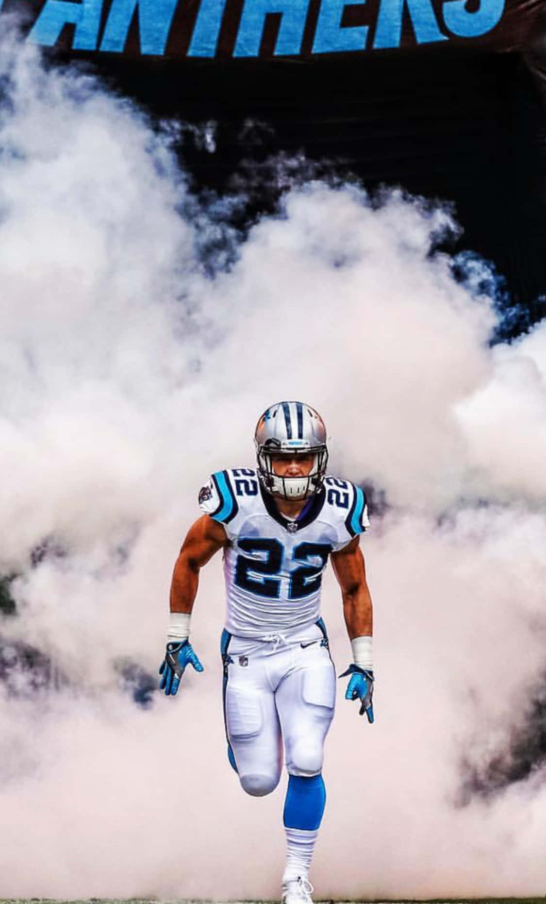 Christian Mccaffrey 桌布 壁紙 — 卡羅萊納黑豹隊美式足球員身穿白色和藍色制服，穿過濃煙，上方有「PANTHERS」橫幅。