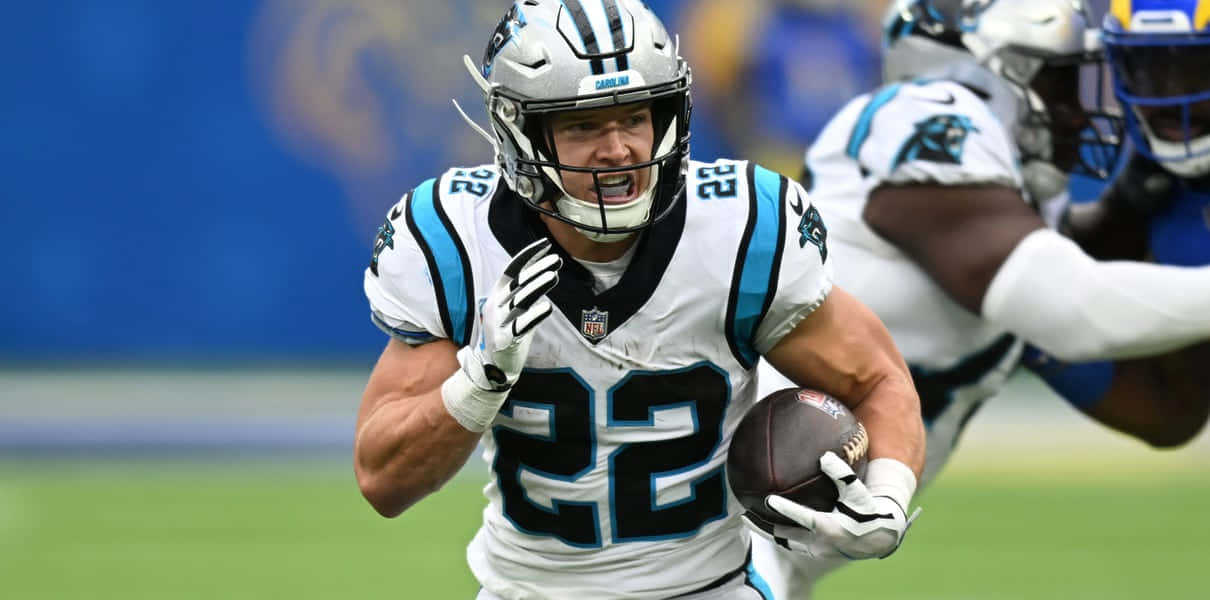 Christian Mccaffrey 桌布 壁紙 — 卡羅萊納黑豹隊身穿白色和藍色制服的美式足球員在綠色球場上持球奔跑，同時被防守球員追趕。