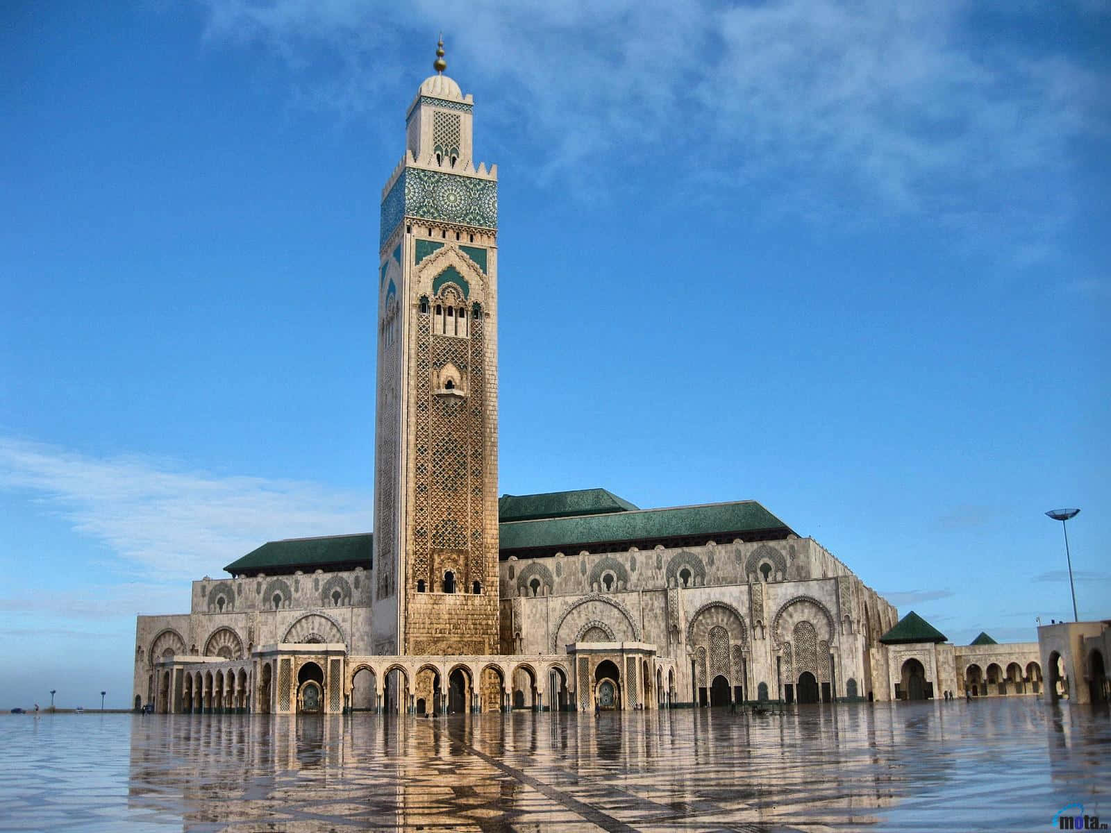 Mosque 桌布 壁紙 — 卡薩布蘭卡的哈桑二世大清真寺在明亮的藍天和零星雲朵下，雄偉地倒映在濕漉漉的廣場上。