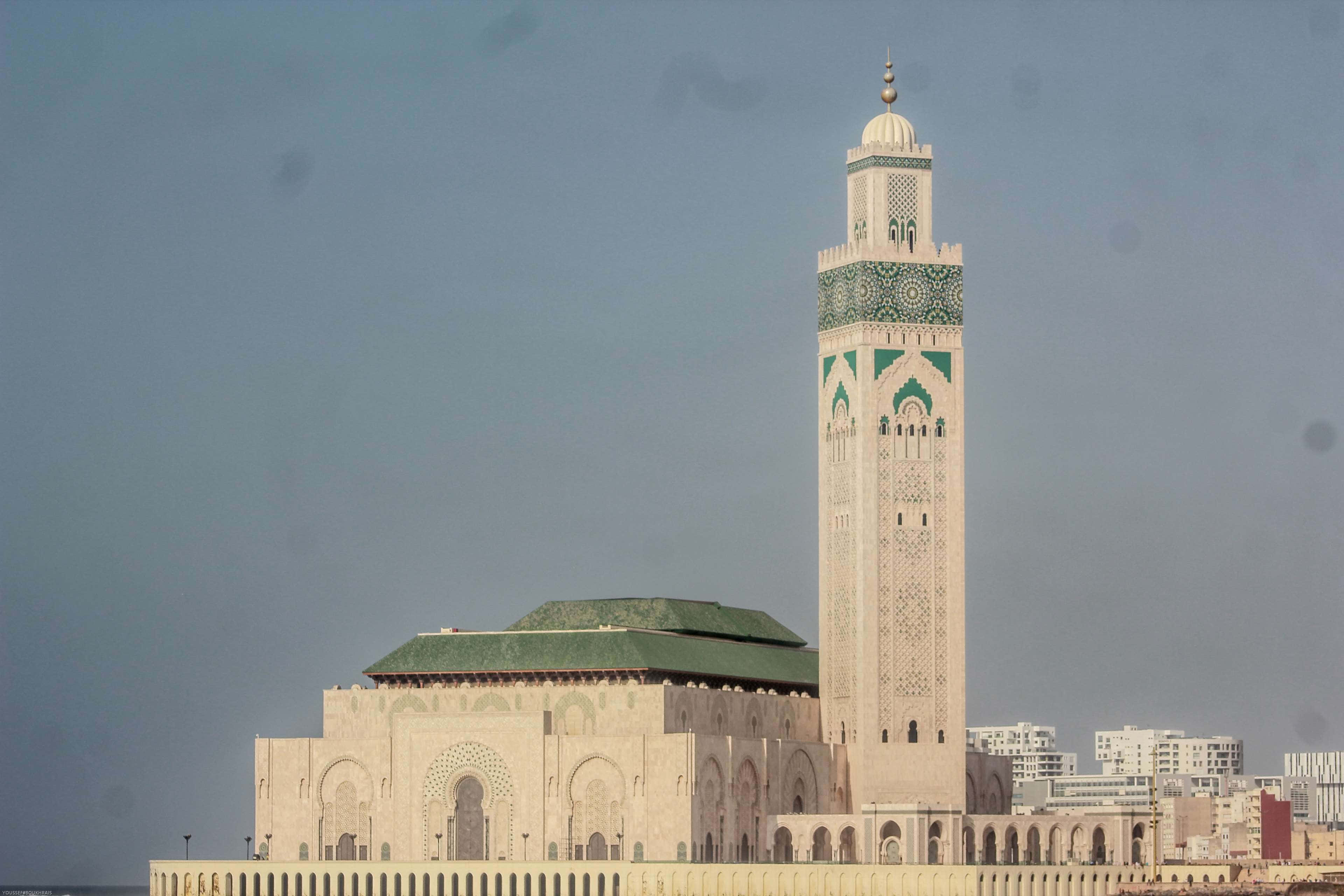 Mosque 桌布 壁紙 — 卡薩布蘭卡的哈桑二世大清真寺高聳入雲，其標誌性宣禮塔和綠色瓦頂在朦朧的天空下格外醒目。