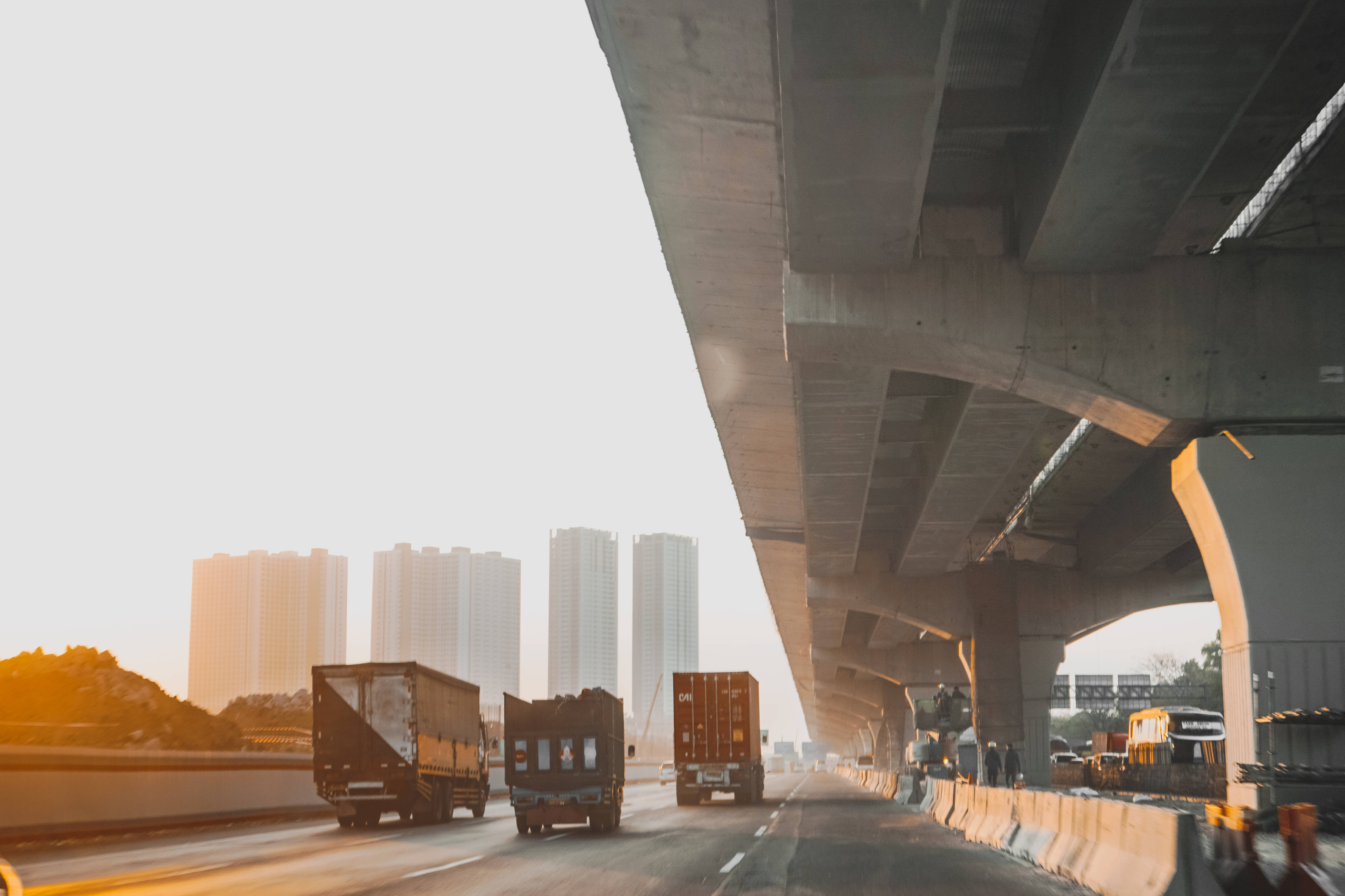 Truck 桌布 壁紙 — 卡車在巨大的混凝土高架橋下行駛，金色的夕陽照耀著遠處的城市天際線。