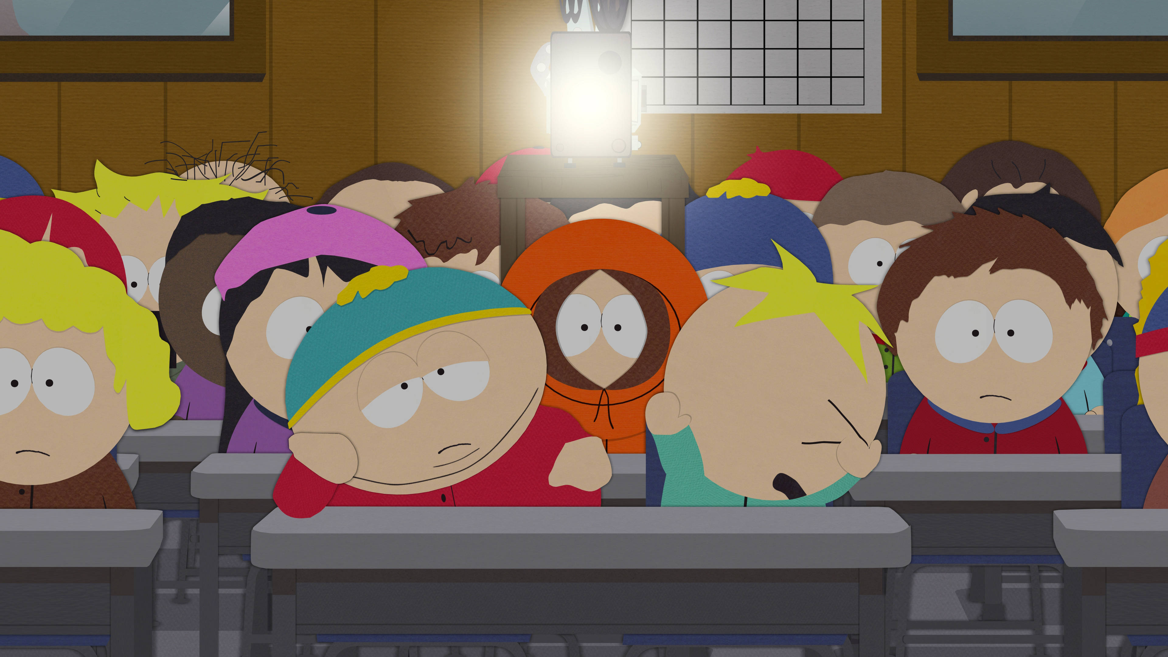 Cartman 桌布 壁紙 — 卡通小孩在教室裡坐在書桌前，在明亮的頭頂燈光下露出無聊或疲倦的表情。