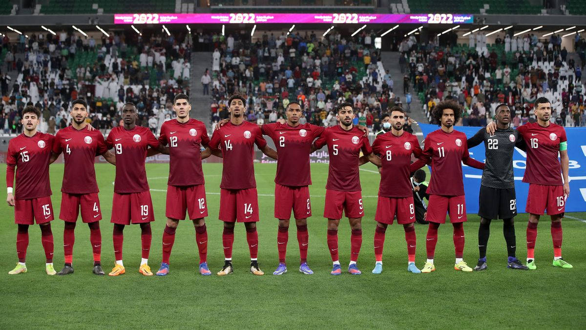 Qatar 桌布 壁紙 — 卡達國家足球隊球員身穿紅色球衣，在球場燈光下於綠色草地上排成一列，背景有球迷。
