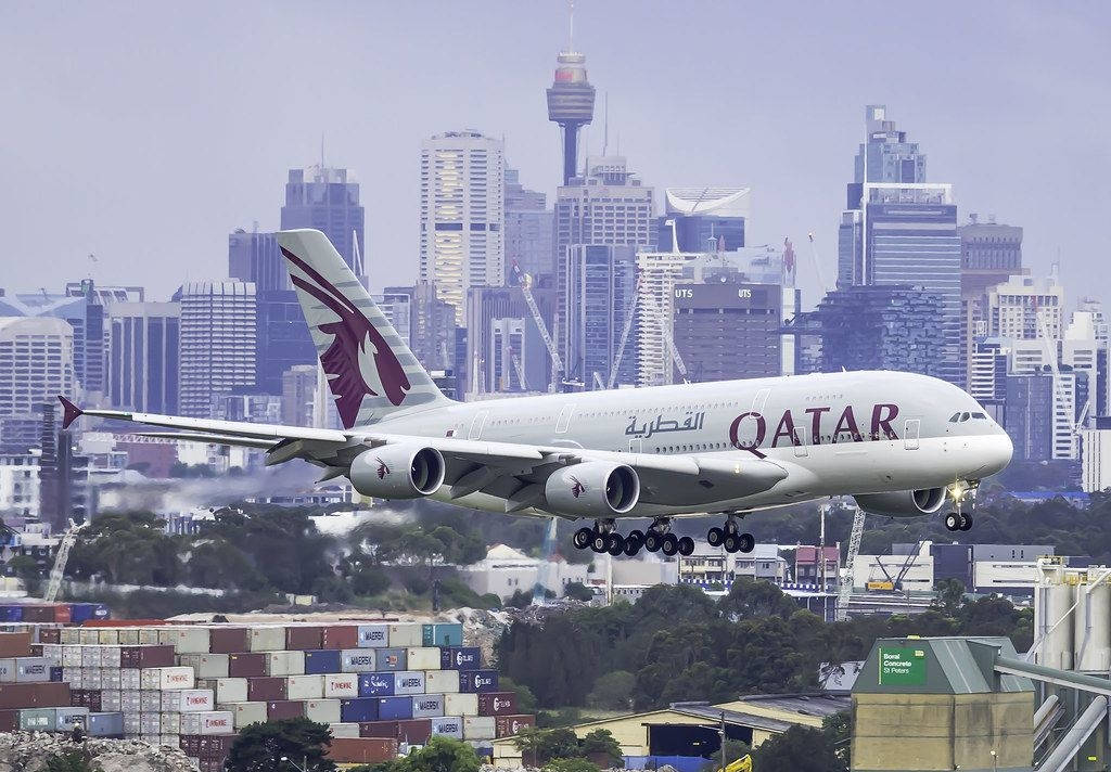 飛機 桌布 壁紙 — 卡達航空空中巴士A380低飛越過堆滿貨櫃的港口，背景是煙霧瀰漫的城市天際線，標誌性的雪梨塔清晰可見。