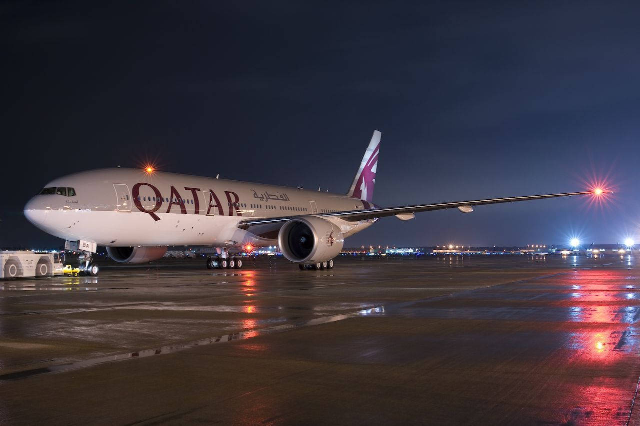 飛機 桌布 壁紙 — 卡達航空飛機在夜燈下於濕滑停機坪閃耀，反射出鮮豔的紅白光芒。